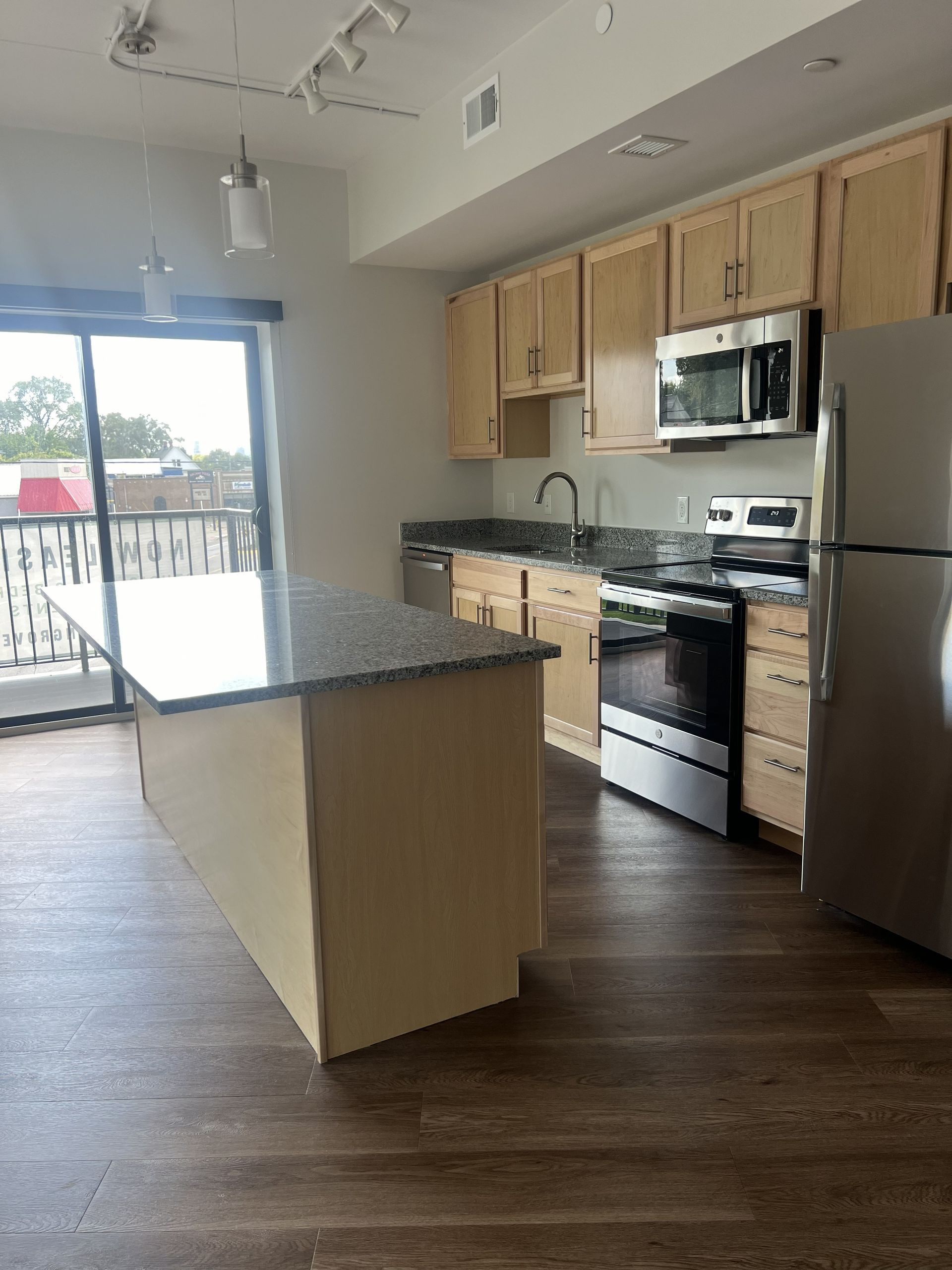 Modern kitchen with granite island, stainless steel appliances, wood cabinets, and sliding glass doors.