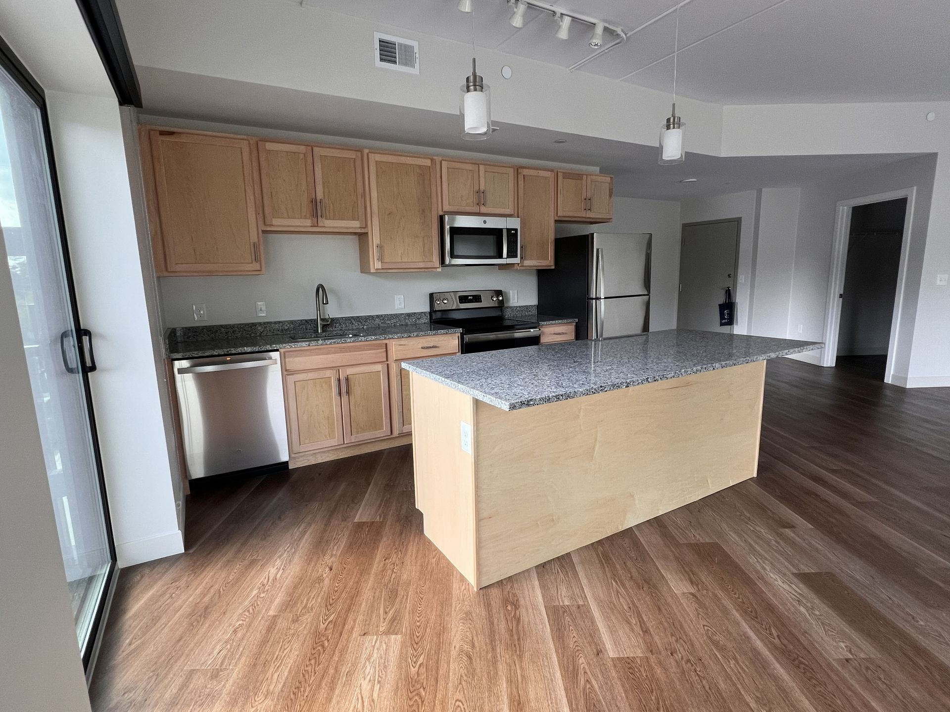 Empty modern kitchen with wood cabinets, stainless appliances, granite island, and hardwood floors