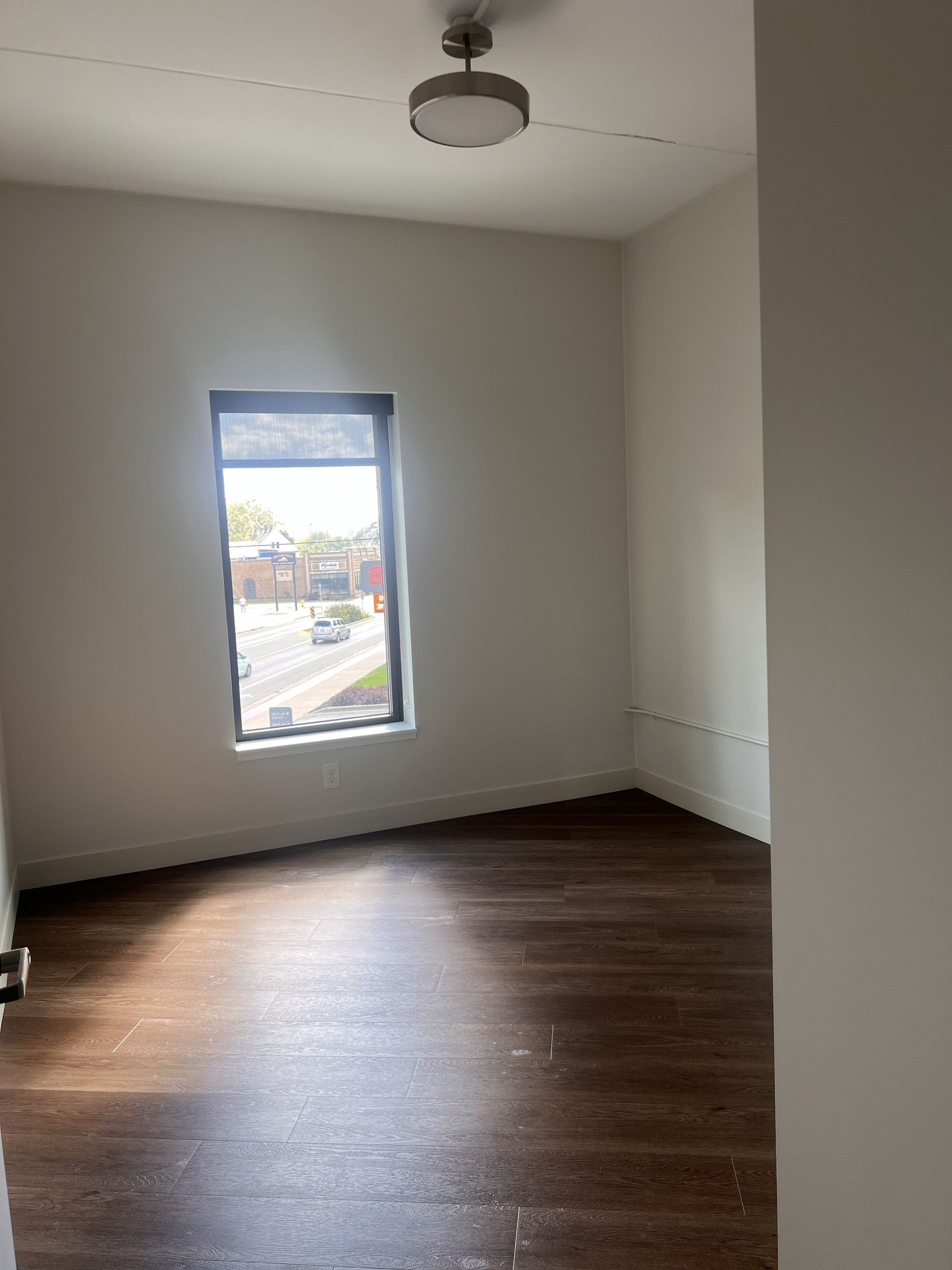 Empty room with dark wood floor, white walls, a window, and a ceiling light fixture.