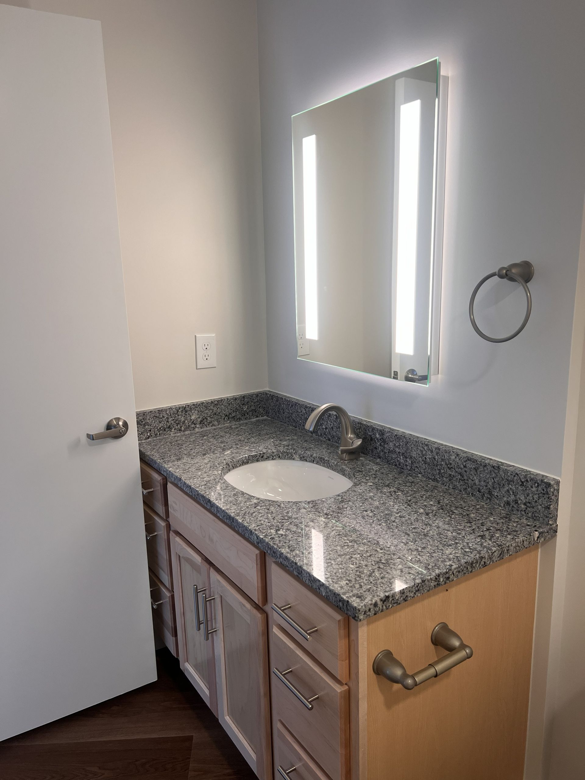 Small bathroom vanity with granite countertop, sink, mirror, and towel ring beside an open door