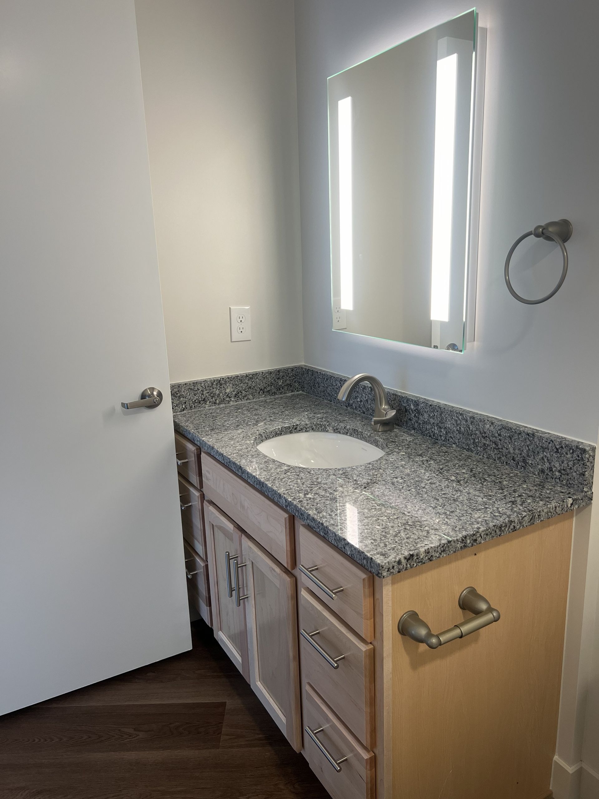 Bathroom vanity with granite countertop, sink, mirror, and towel ring beside a partially open door