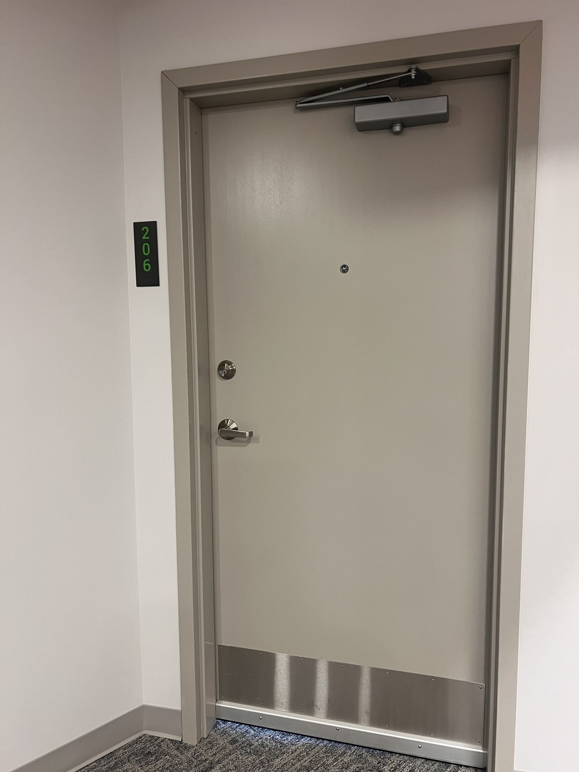 Closed gray metal door in a hallway with a push bar and green exit sign on the wall