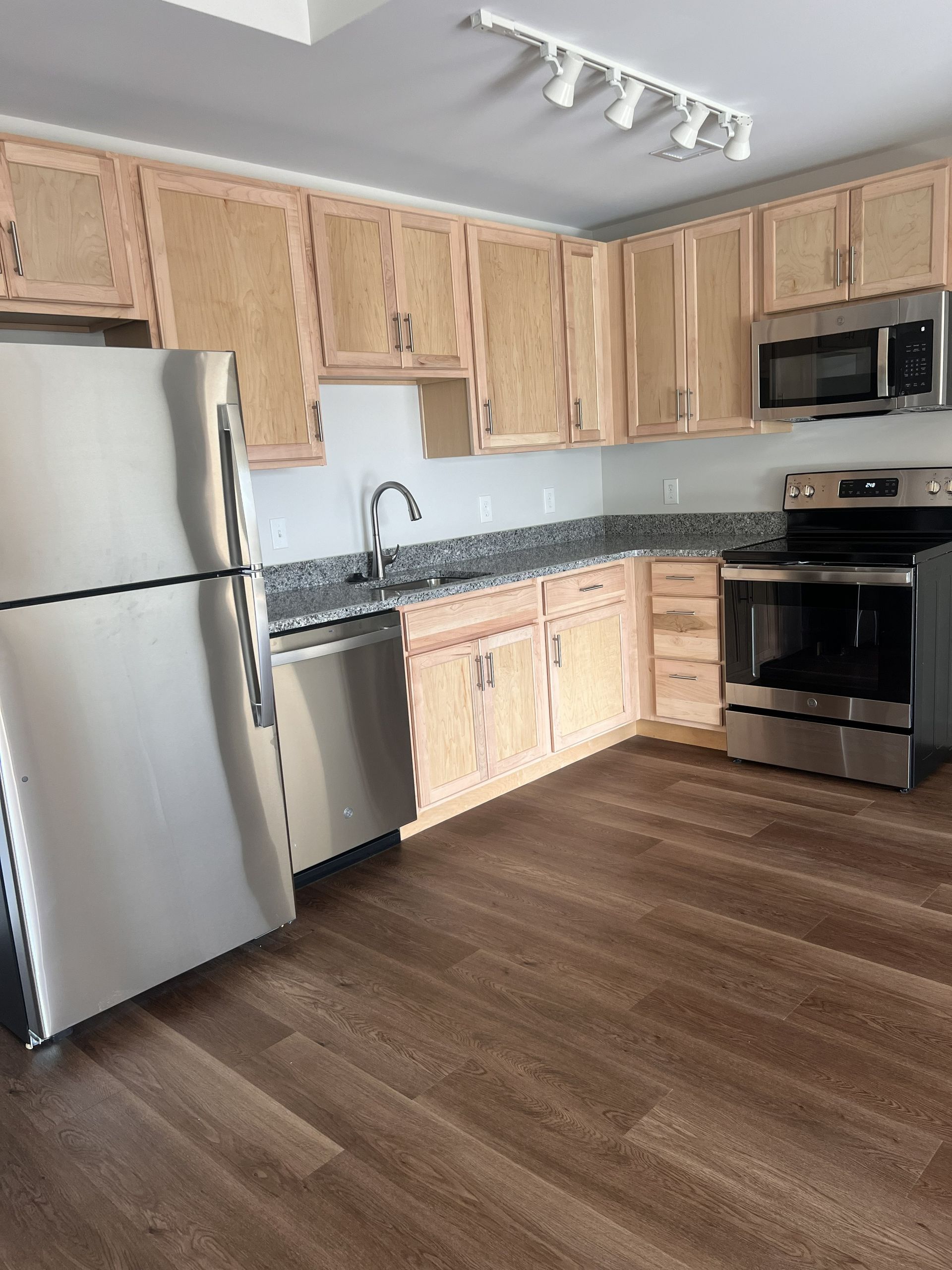 Modern kitchen with stainless steel appliances, light wood cabinets, and dark wood flooring.