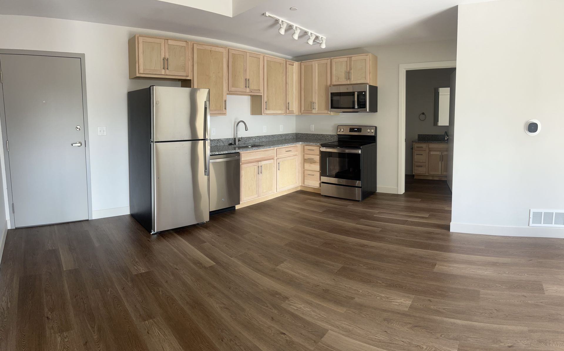 Empty modern kitchen with light wood cabinets, stainless appliances, and dark wood flooring in open living space