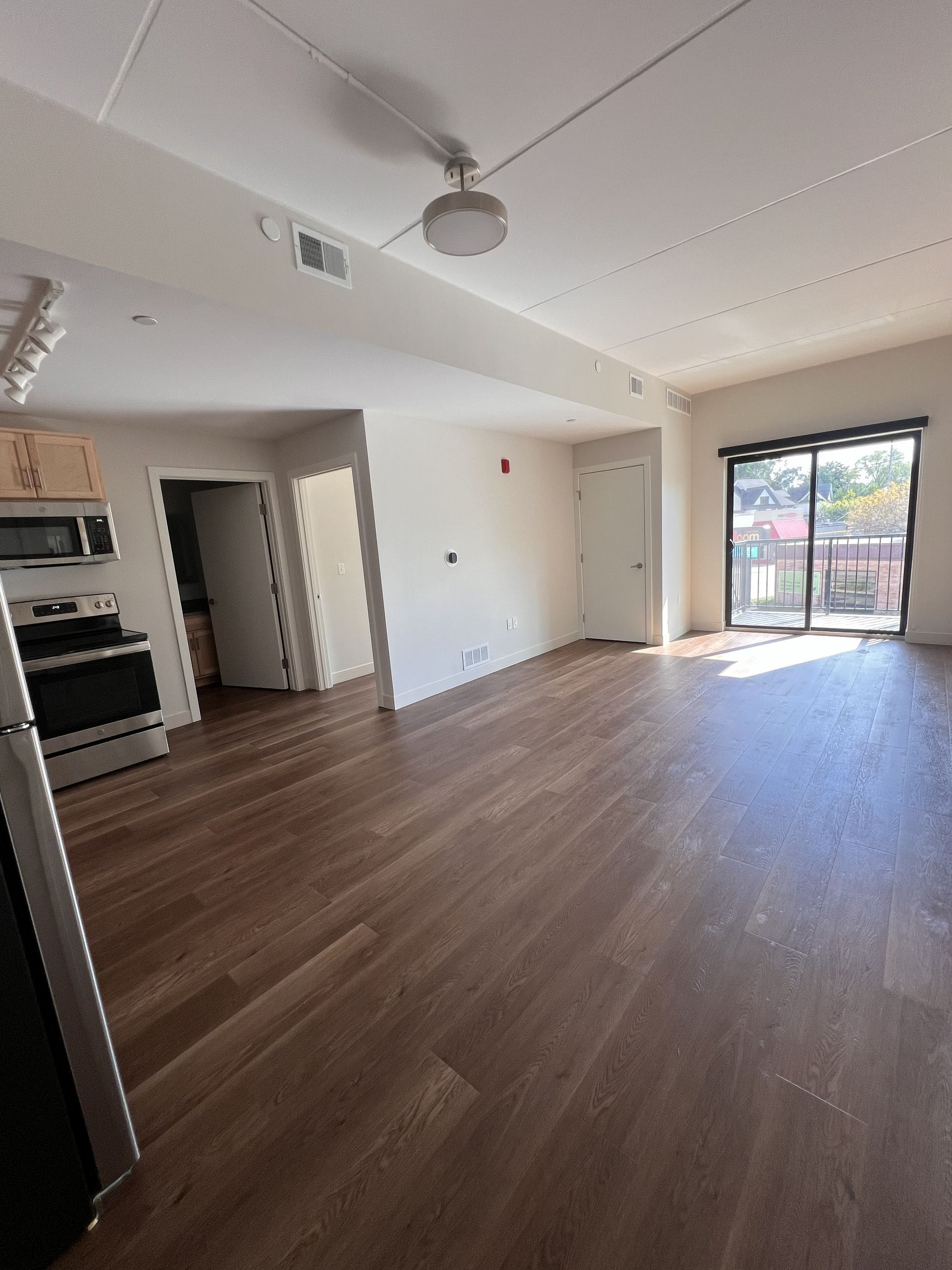 Empty living room with wood floors, ceiling fan, and sliding glass doors opening to a patio.