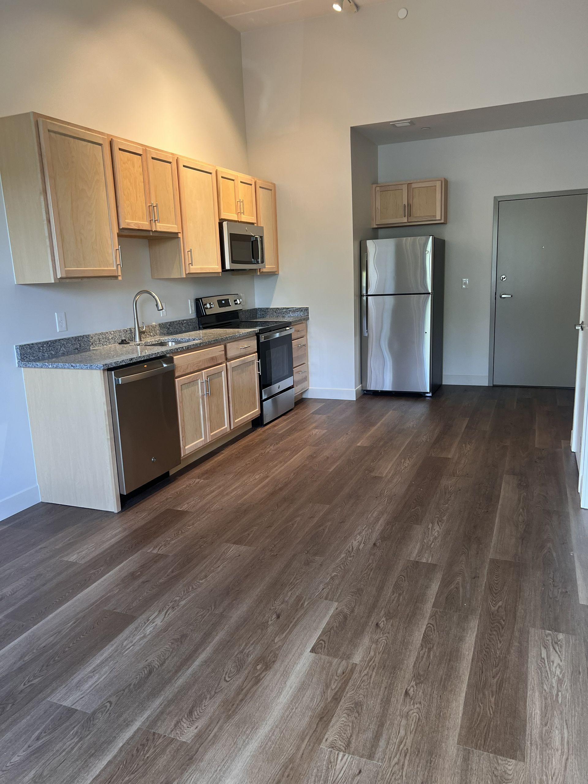 Empty kitchen with wood cabinets, stainless steel appliances, granite counters, and dark wood flooring