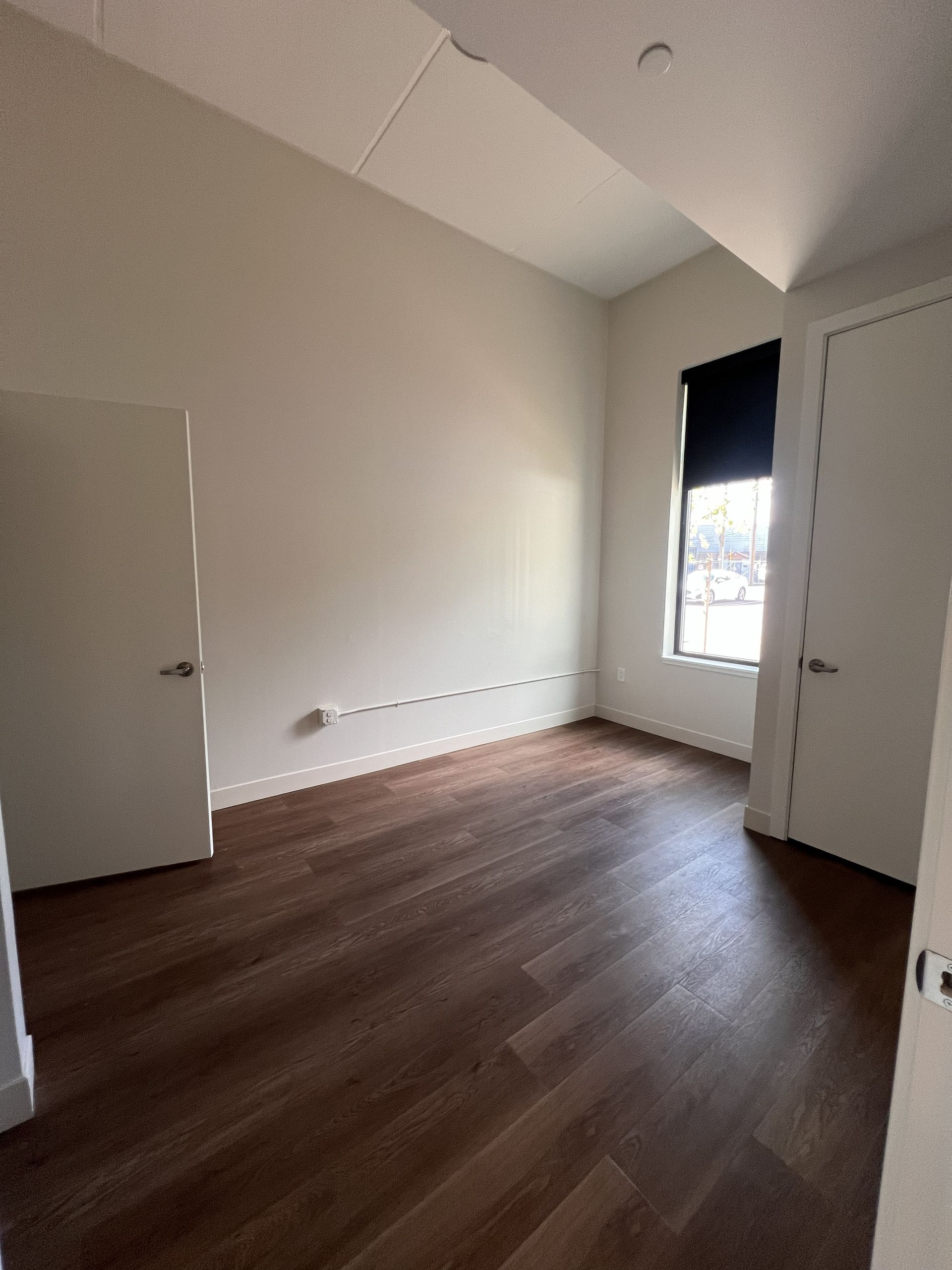 Empty beige room with wood floors, open doors, and a window letting in light.