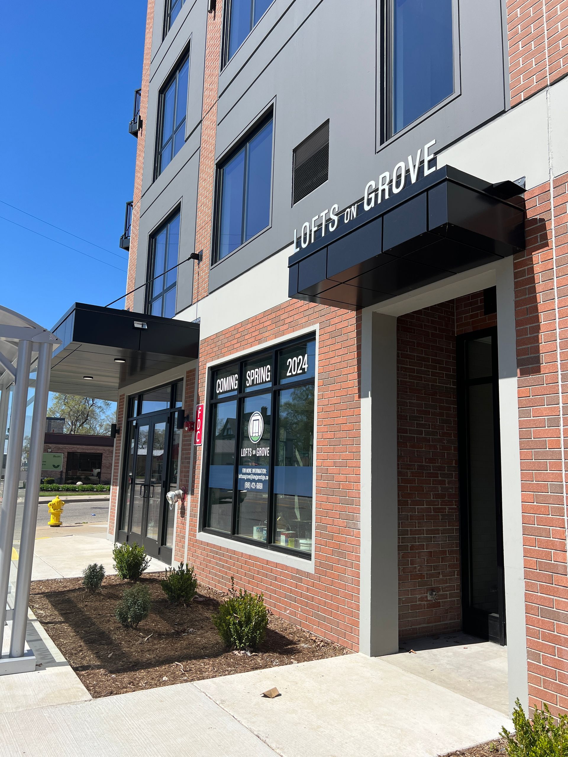 Storefront entrance with brick facade, glass doors, and black awning on a sunny street.
