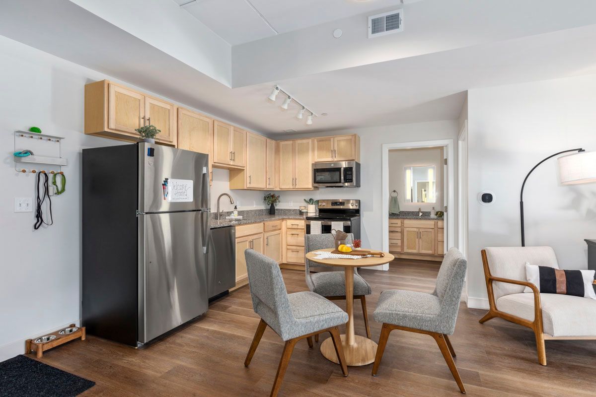 Bright kitchen and dining area with stainless steel appliances, wood cabinets, and gray chairs