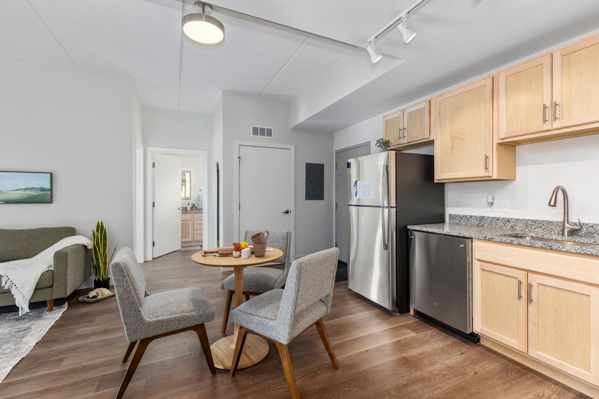 Modern apartment kitchen and dining area with wood cabinets, stainless appliances, and a small round table with chairs.