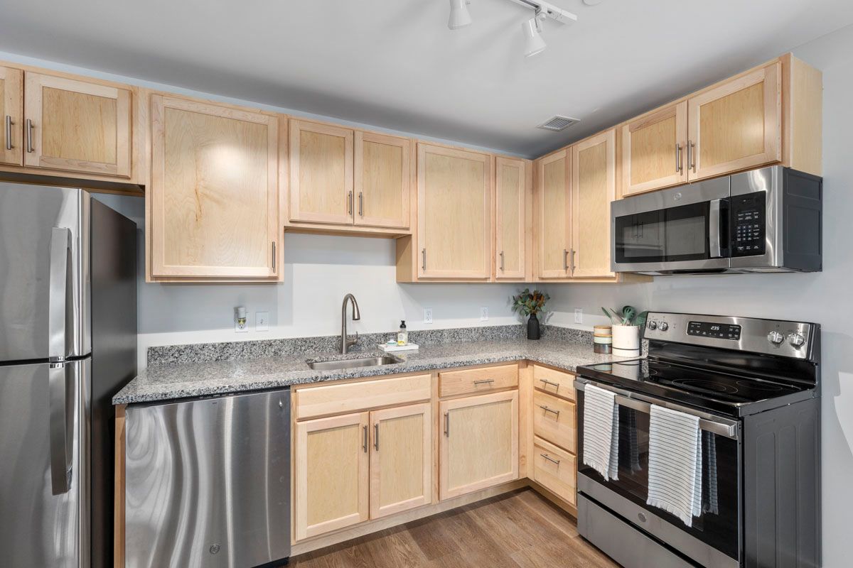 Modern kitchen with light wood cabinets, stainless steel appliances, granite counters, and tiled backsplash