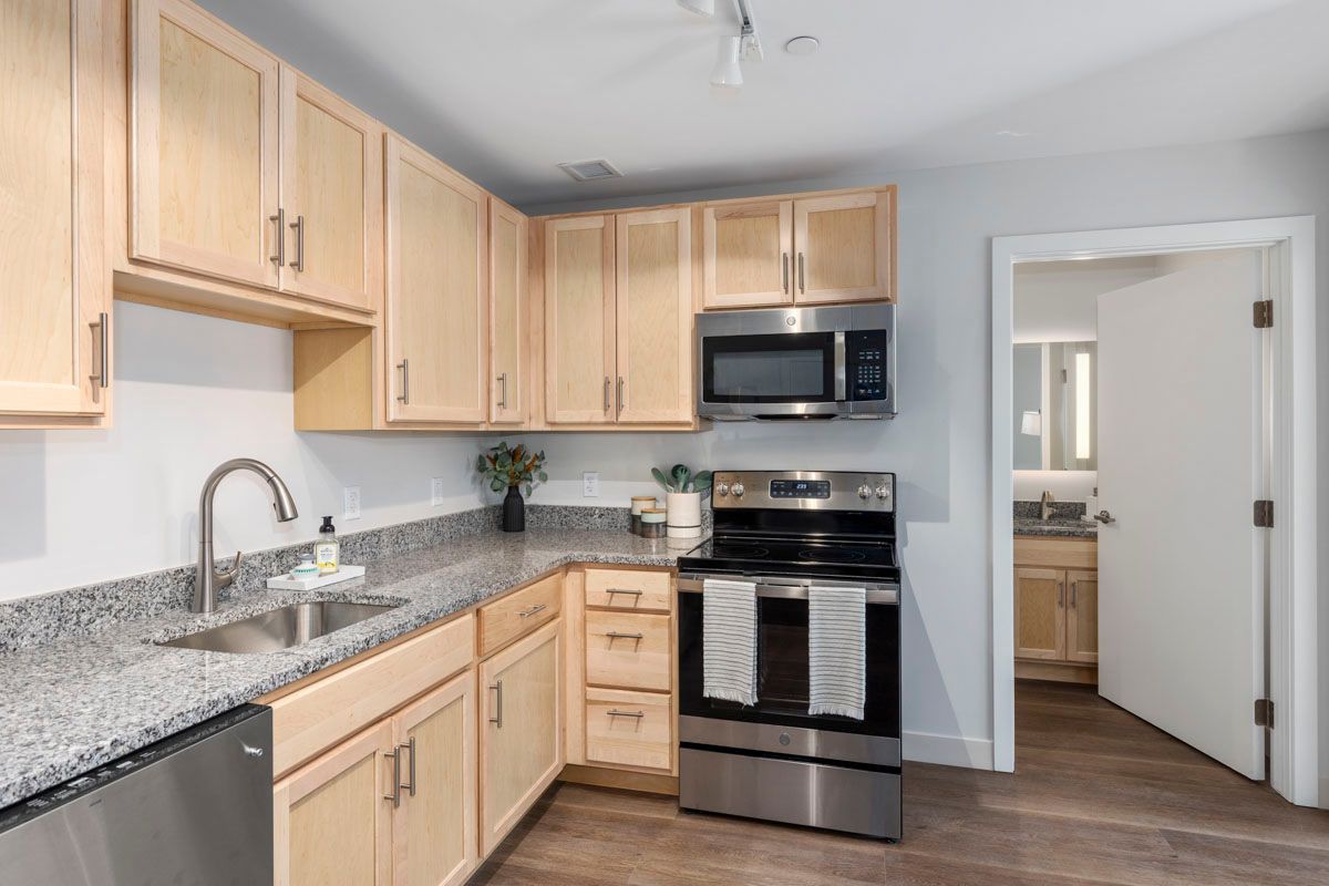 Bright kitchen with light wood cabinets, granite counters, stainless appliances, and gray walls