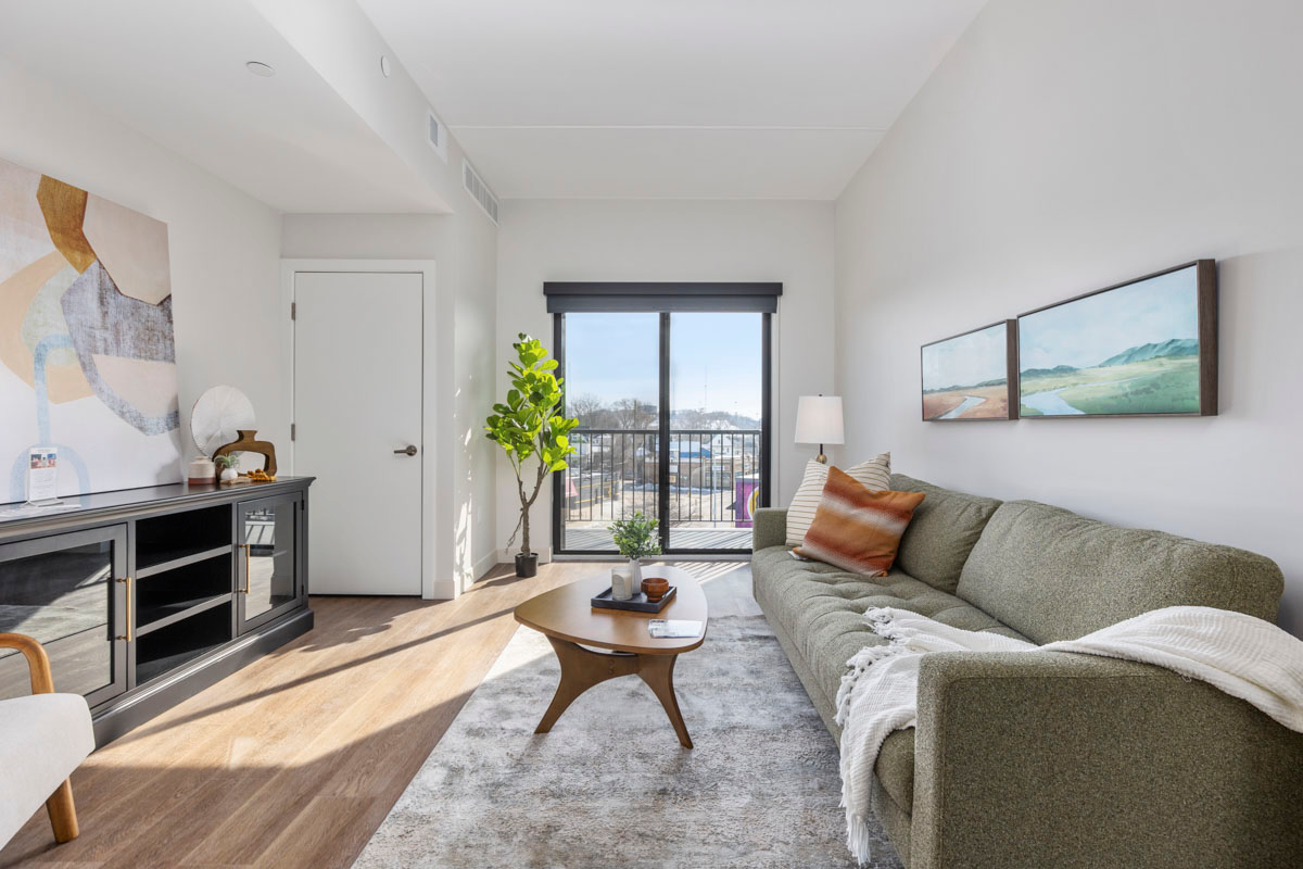 Bright living room with a gray sofa, coffee table, wall art, and sunlight through a sliding glass door.