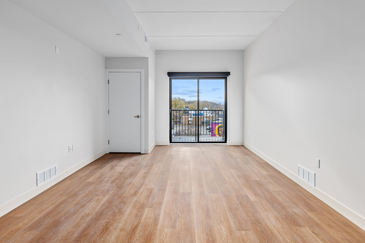 Empty modern room with light wood floors, white walls, and a balcony door at the far end.