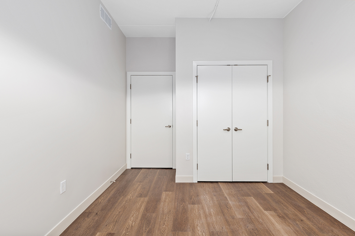 Empty white bedroom with wood floor and two closed doors