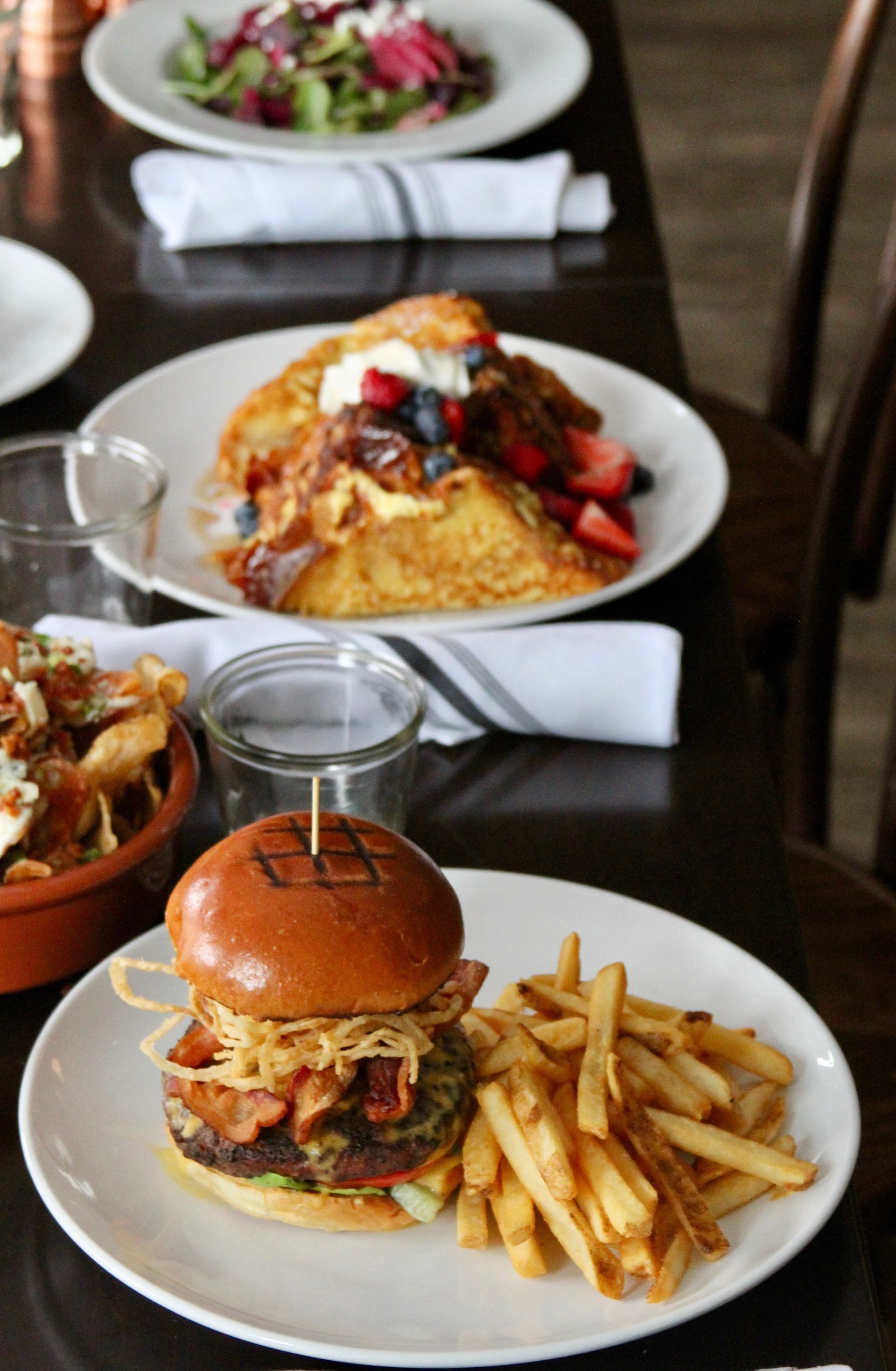 Burger and fries on a white plate at a restaurant table, with other plated dishes in the background