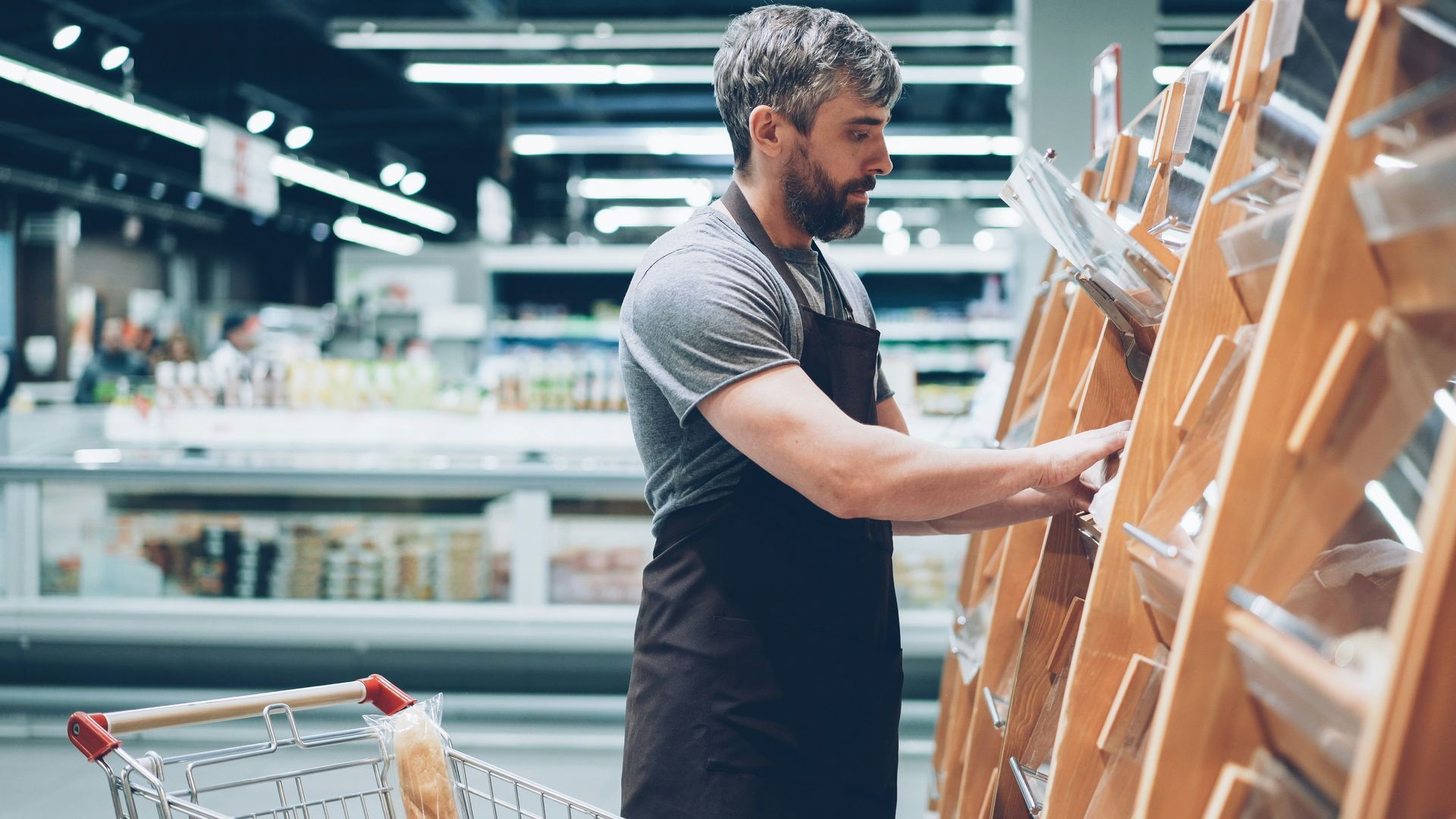 Man stocking bread in a grocery store aisle beside a shopping cart
