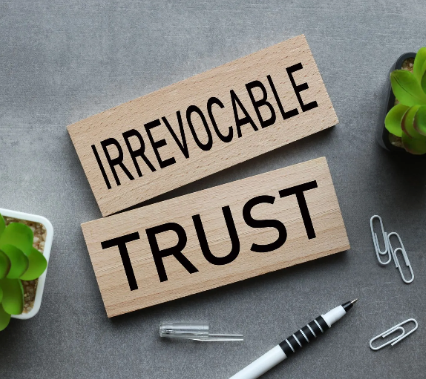 Irrevocable trust blocks on a gray desk with paper clips, pen, and small succulents