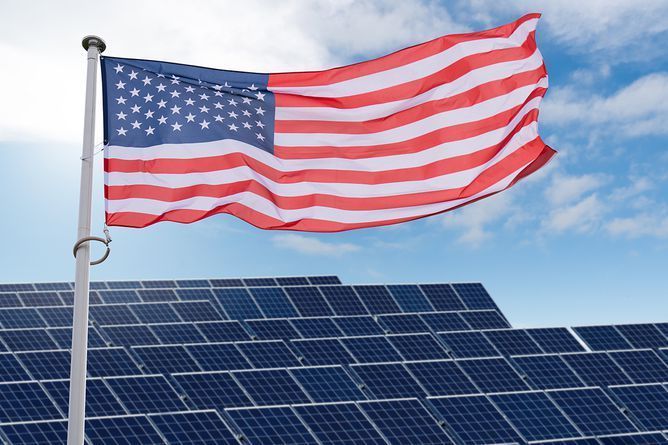 U.S. flag waving above solar panels against a blue sky