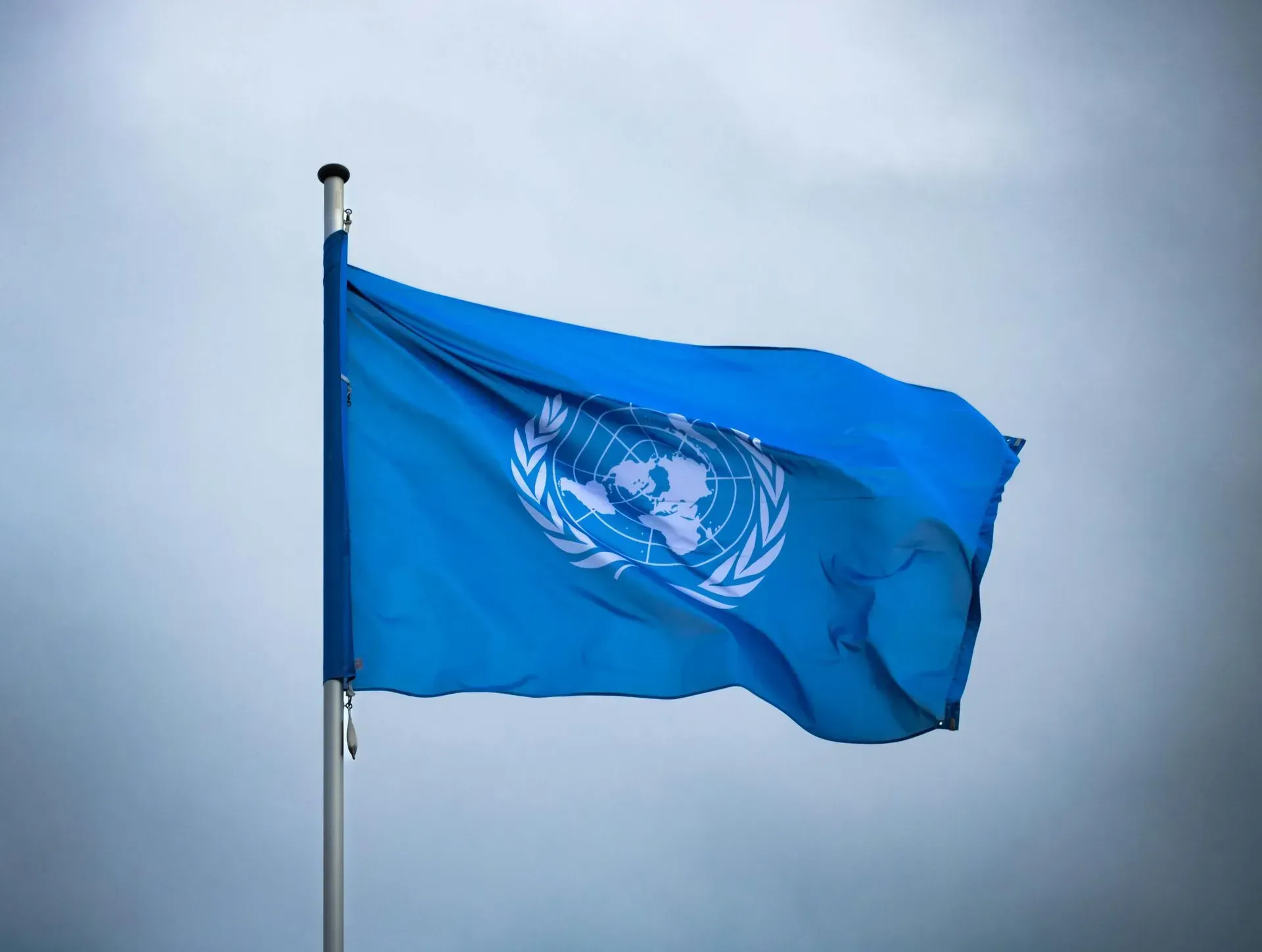 Blue United Nations flag waving on a pole against a cloudy sky