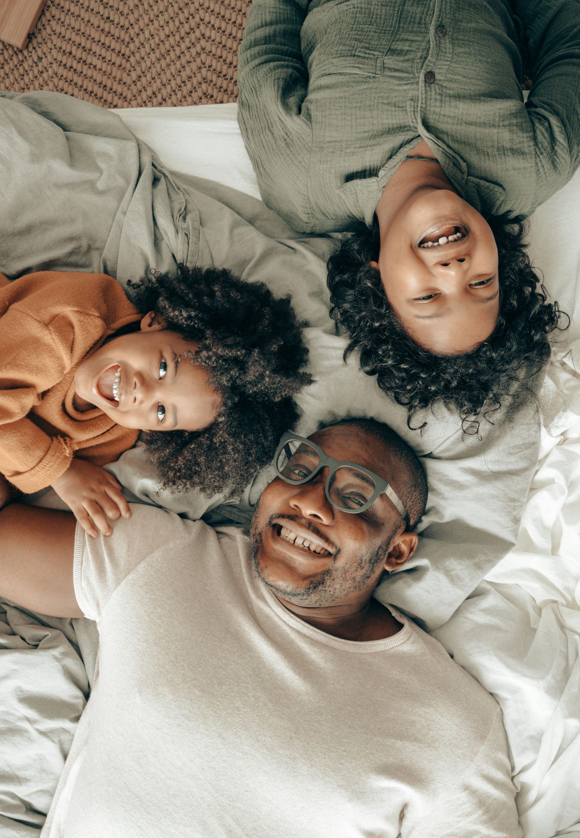 Three people lying on a bed, smiling up at the camera in cozy sweaters