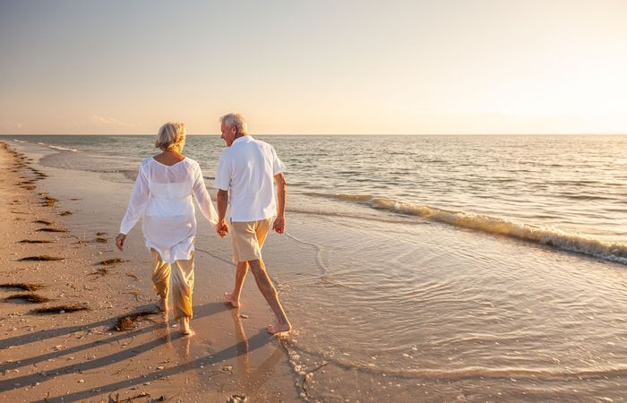 Couple walking hand in hand along a sandy beach at sunset, with gentle waves and warm golden light