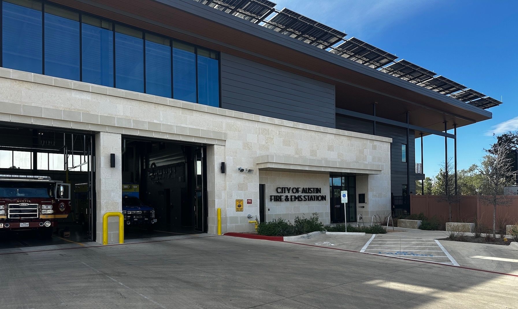 Industrial building exterior with open garage bay, sign, and parked vehicles under a bright blue sky