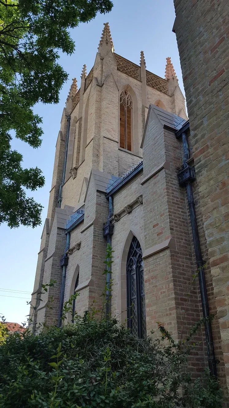 Tall stone church tower with pointed arches, seen from below against a blue sky and trees
