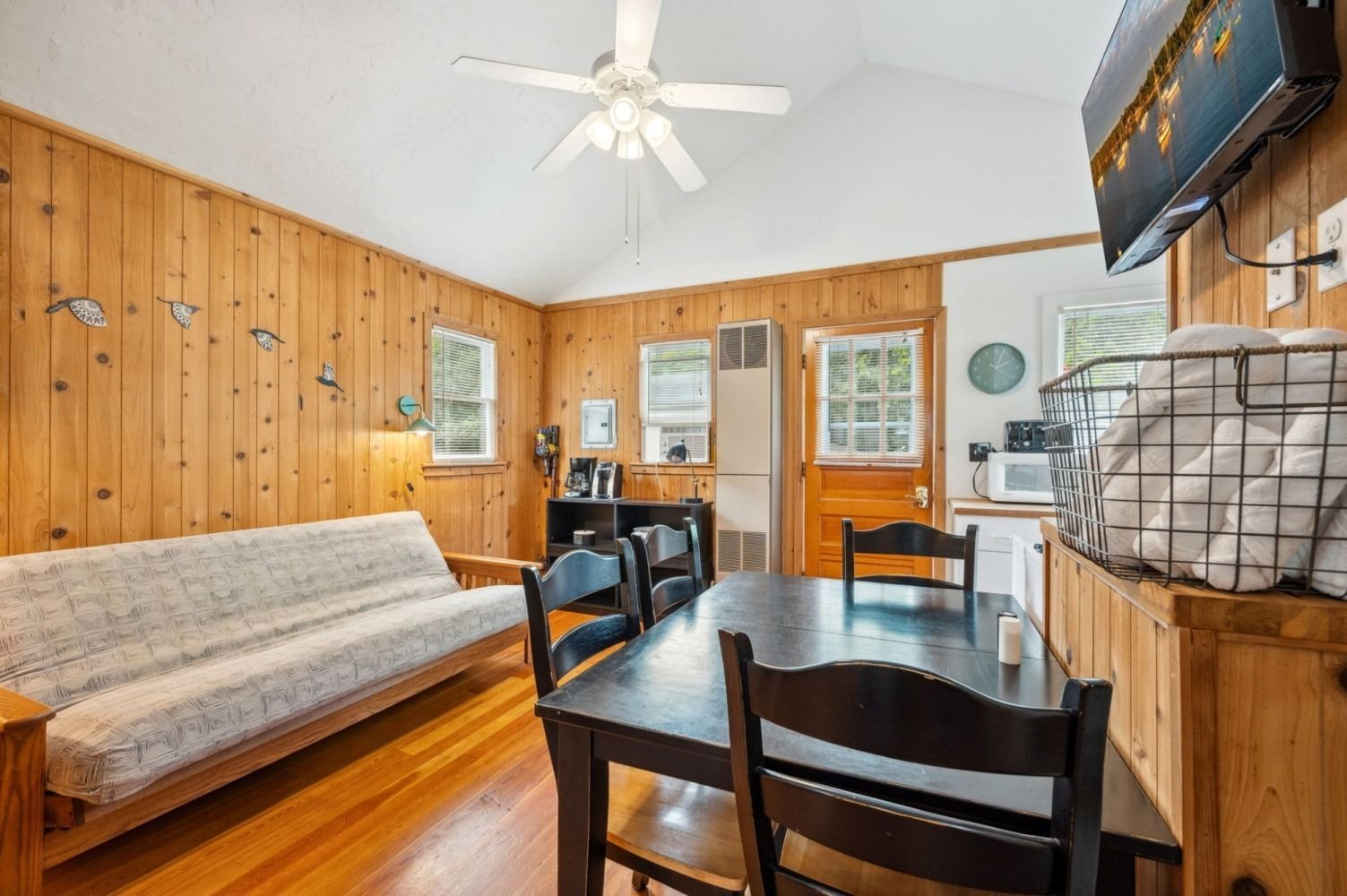 Cozy cabin interior with wood paneling, futon, dining table, and mounted TV.