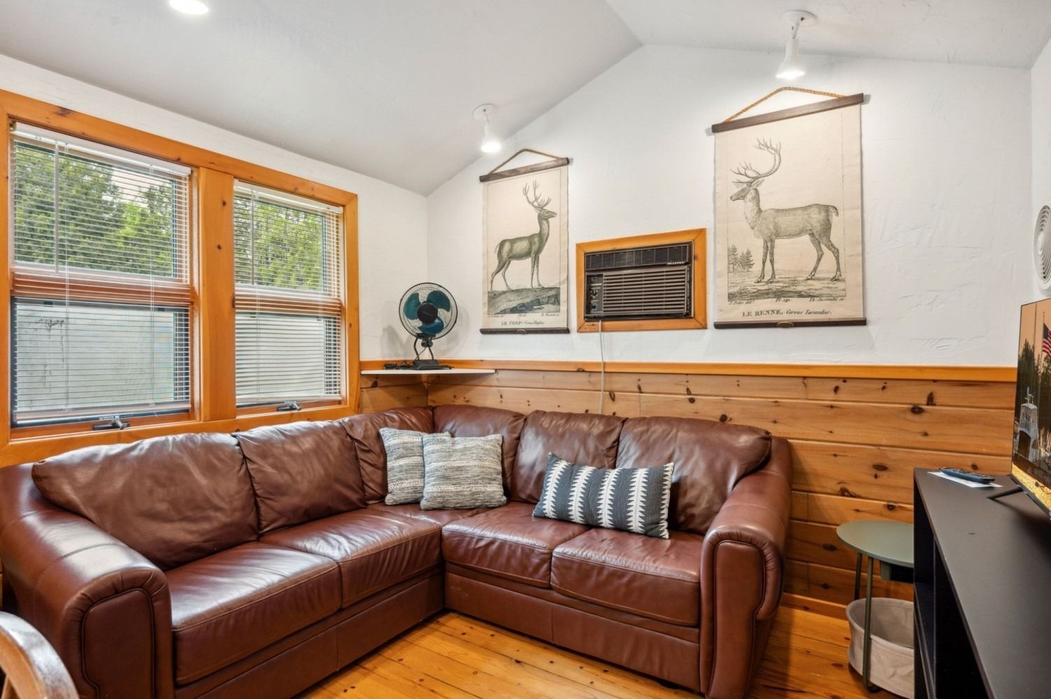 Living room with leather sectional, wood paneling, artwork, and a window.