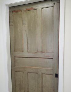 A closed, weathered gray paneled door set within a white door frame.