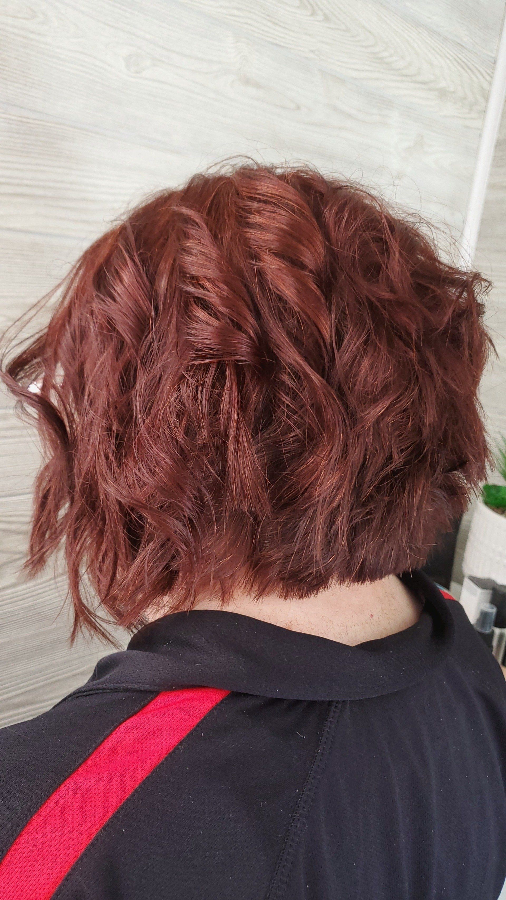Person with auburn, wavy bob haircut, wearing a black top with red stripes.