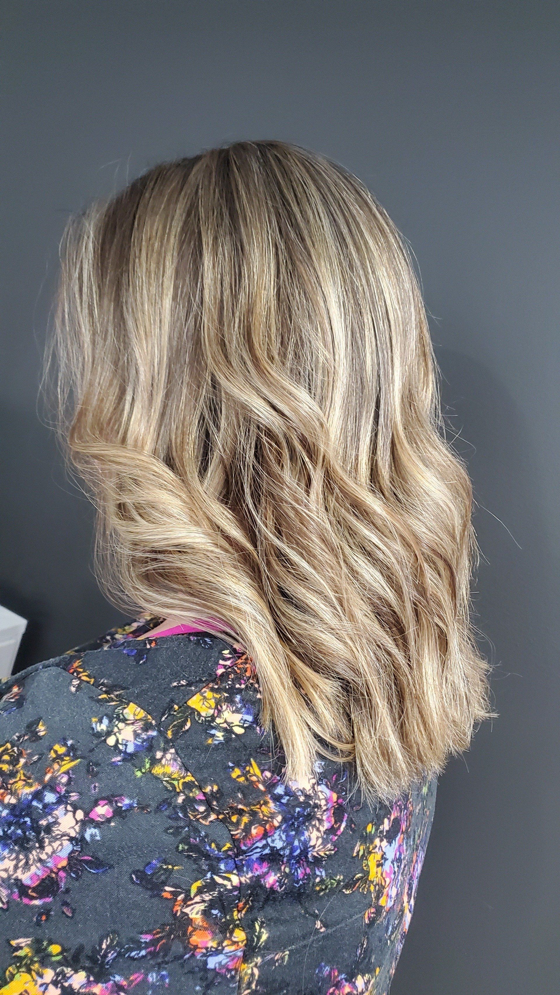 Woman with shoulder-length wavy blonde and light brown highlighted hair, wearing a patterned floral top.