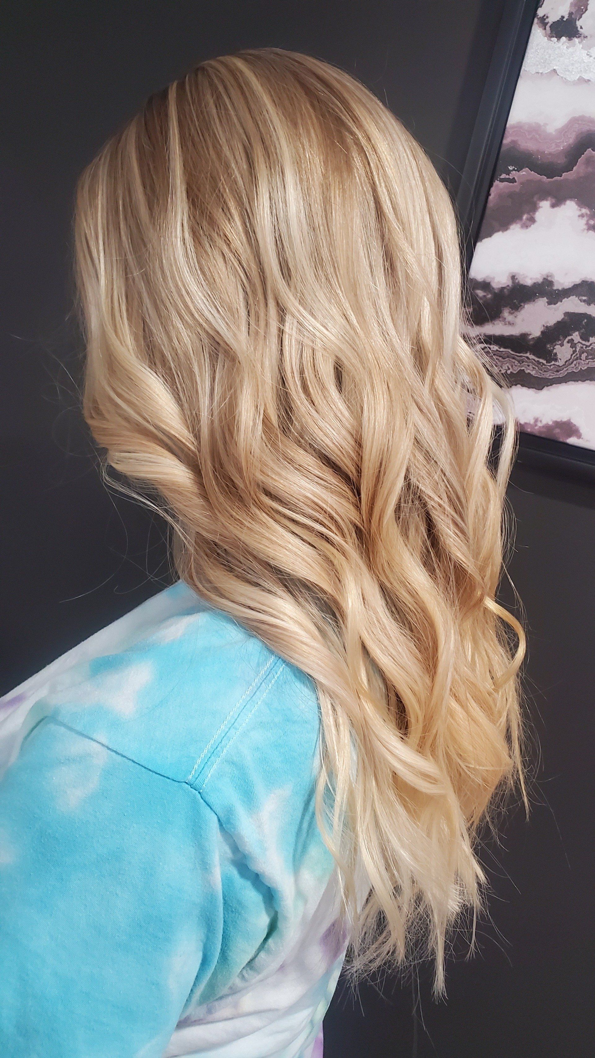 Woman with long, wavy blonde hair; wearing a blue and white tie-dye top.