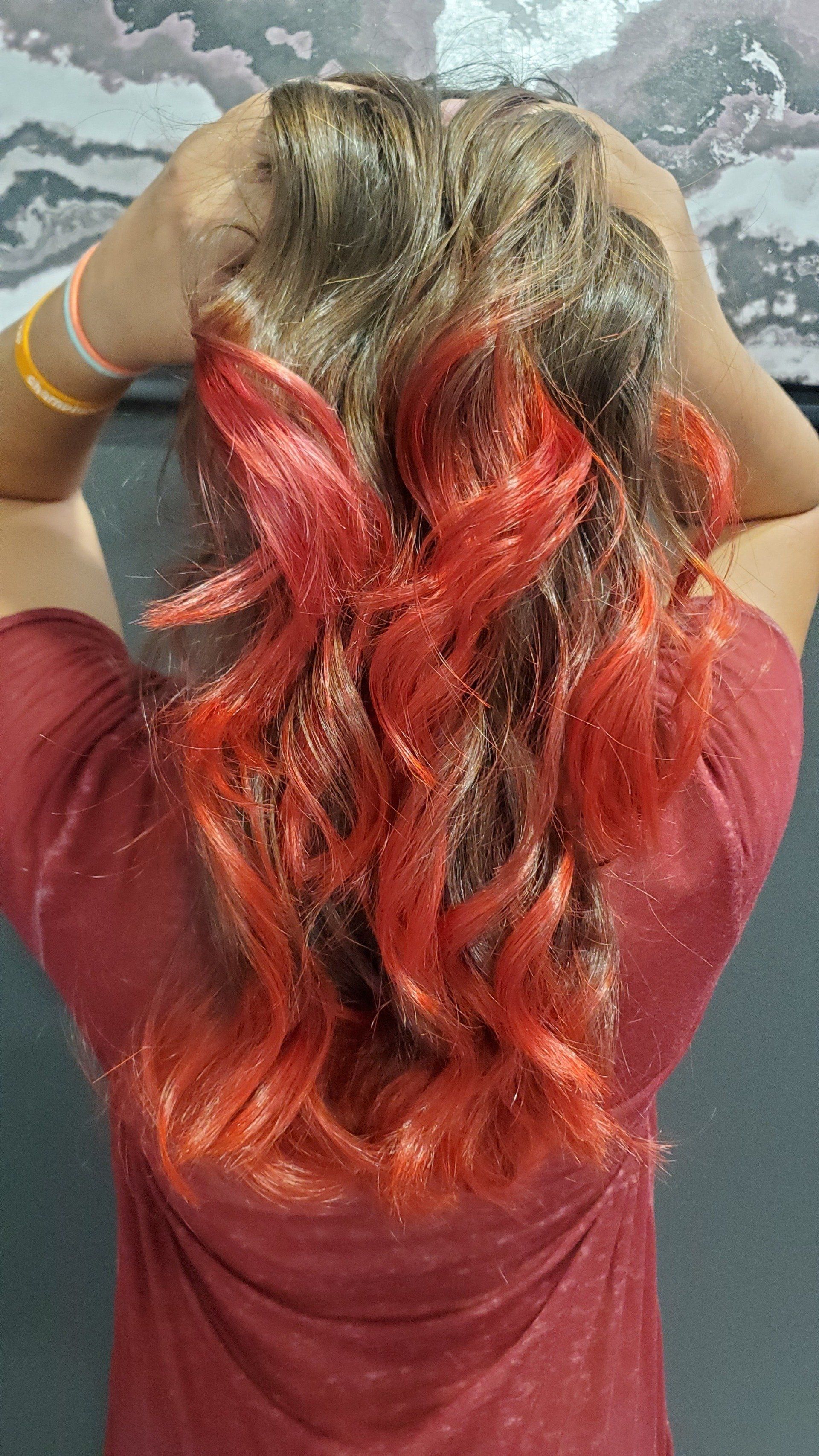 Person with wavy brown hair, with red highlights, arms raised.