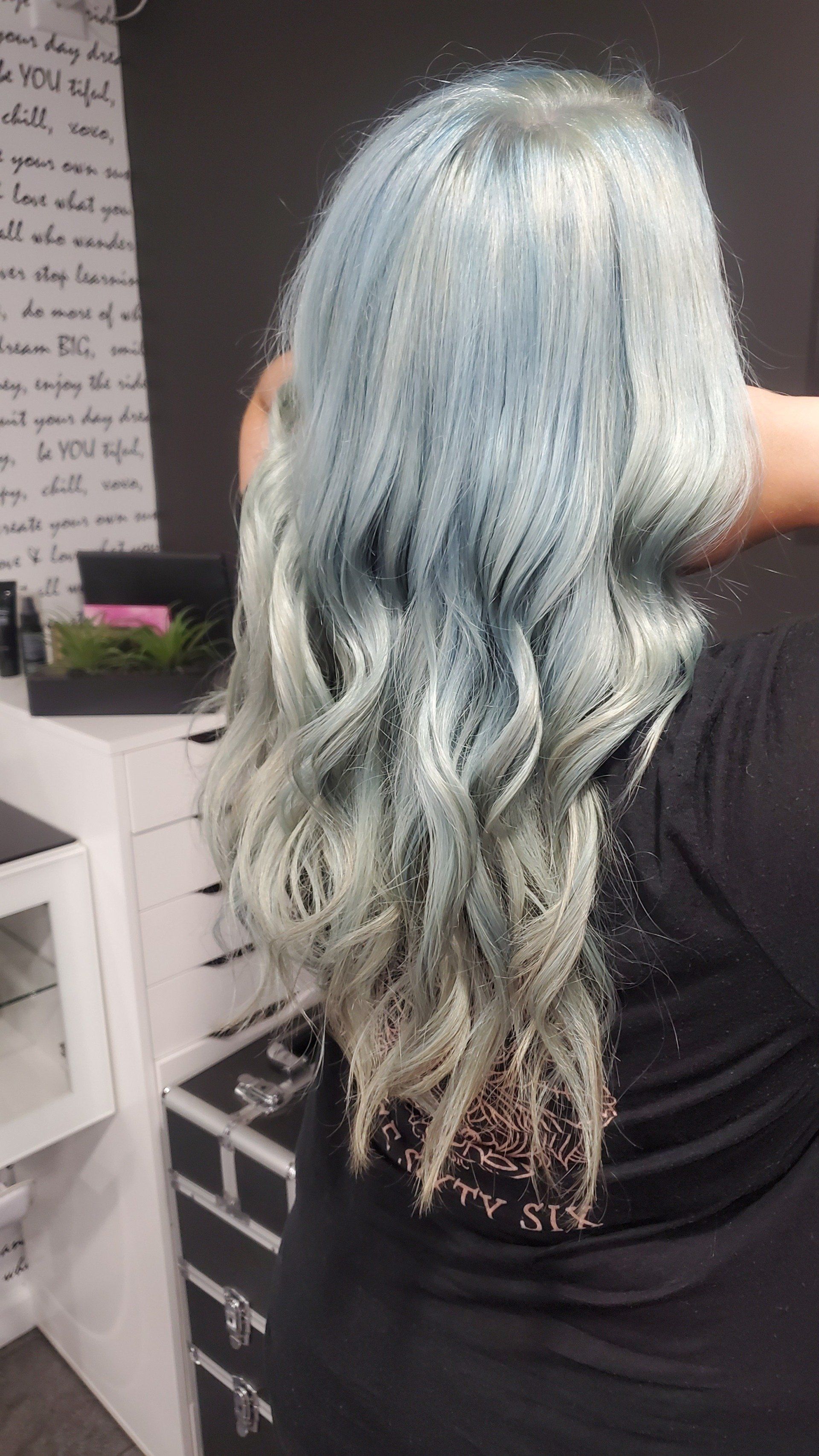 Woman with long wavy blue and silver hair, back view, salon setting.