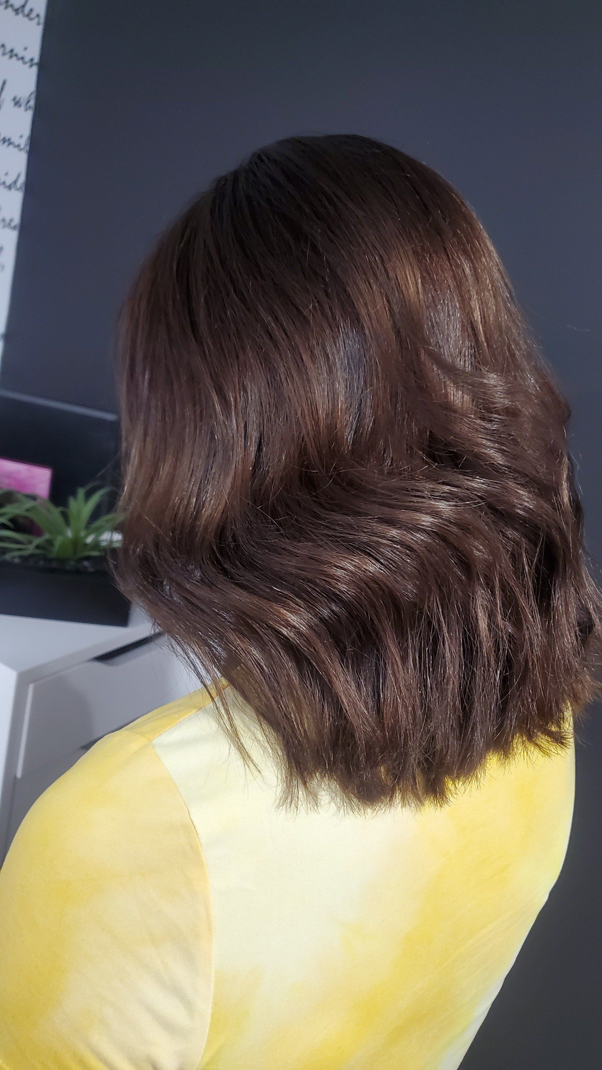 Woman with brown, layered hair; wearing a yellow shirt, in a salon setting.
