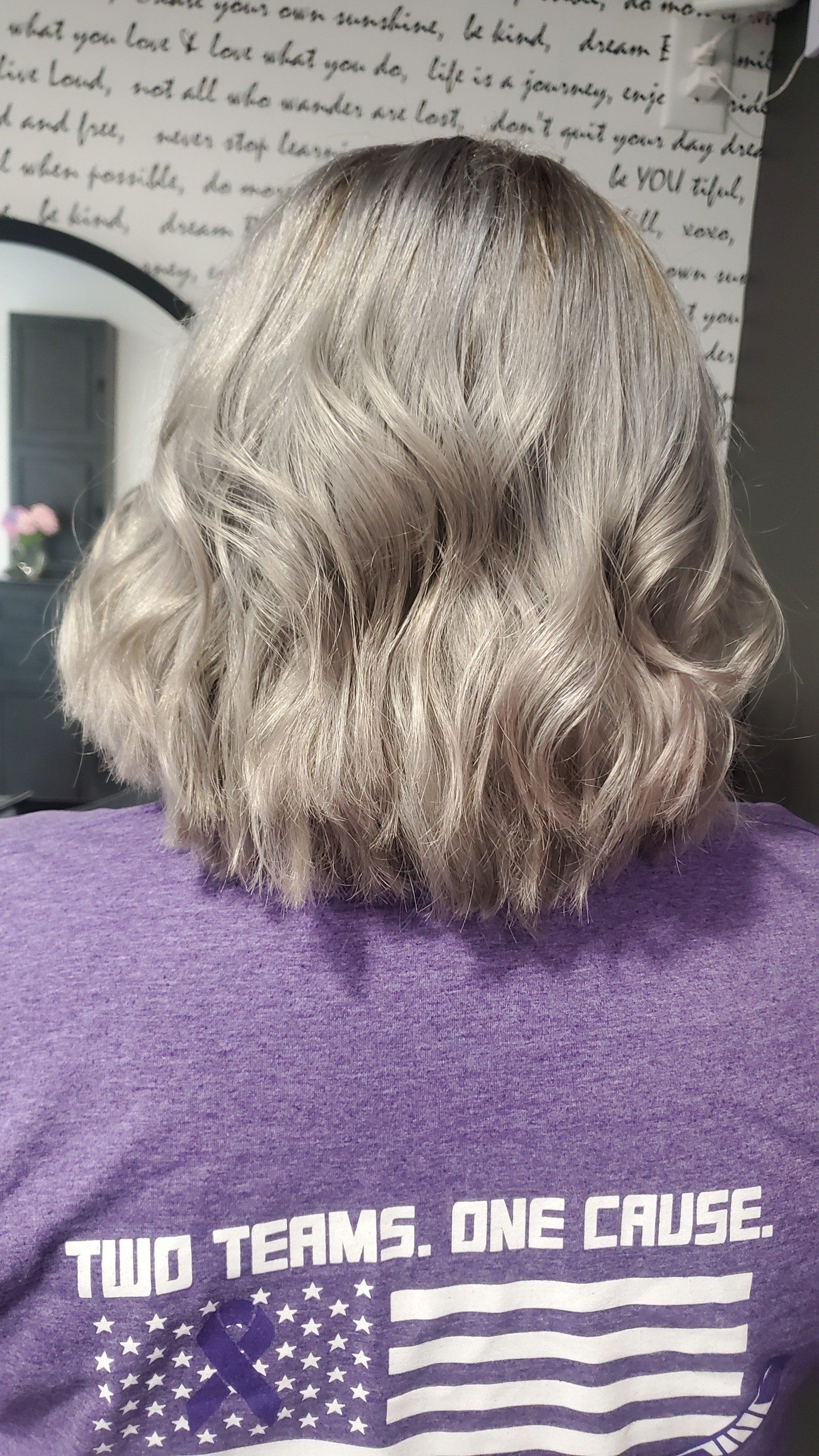 Person wearing a purple shirt with silver wavy bobbed hair. Background shows text and a mirror.