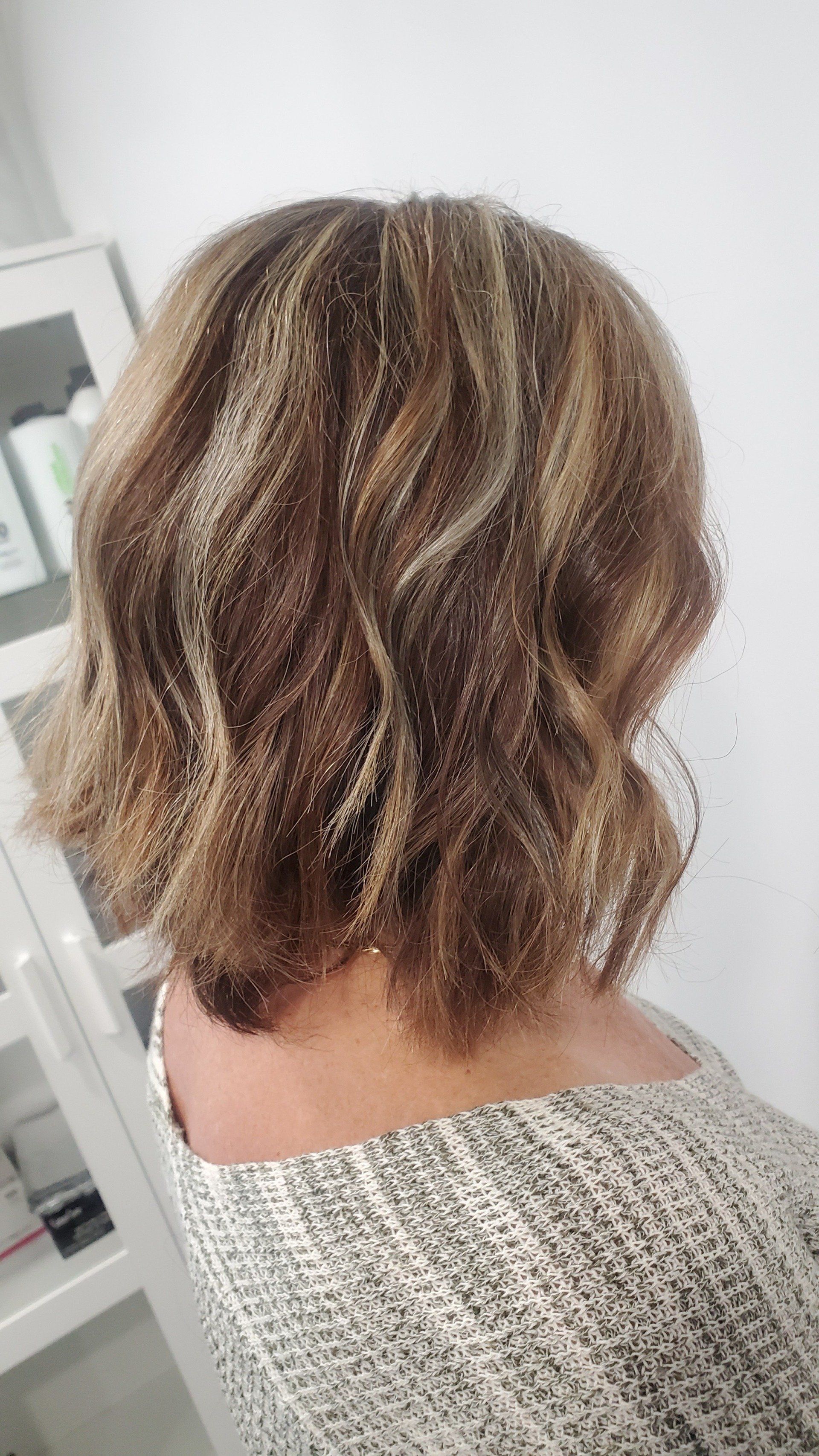 Shoulder-length wavy brown hair with blonde highlights. Person wearing a gray and white patterned top.