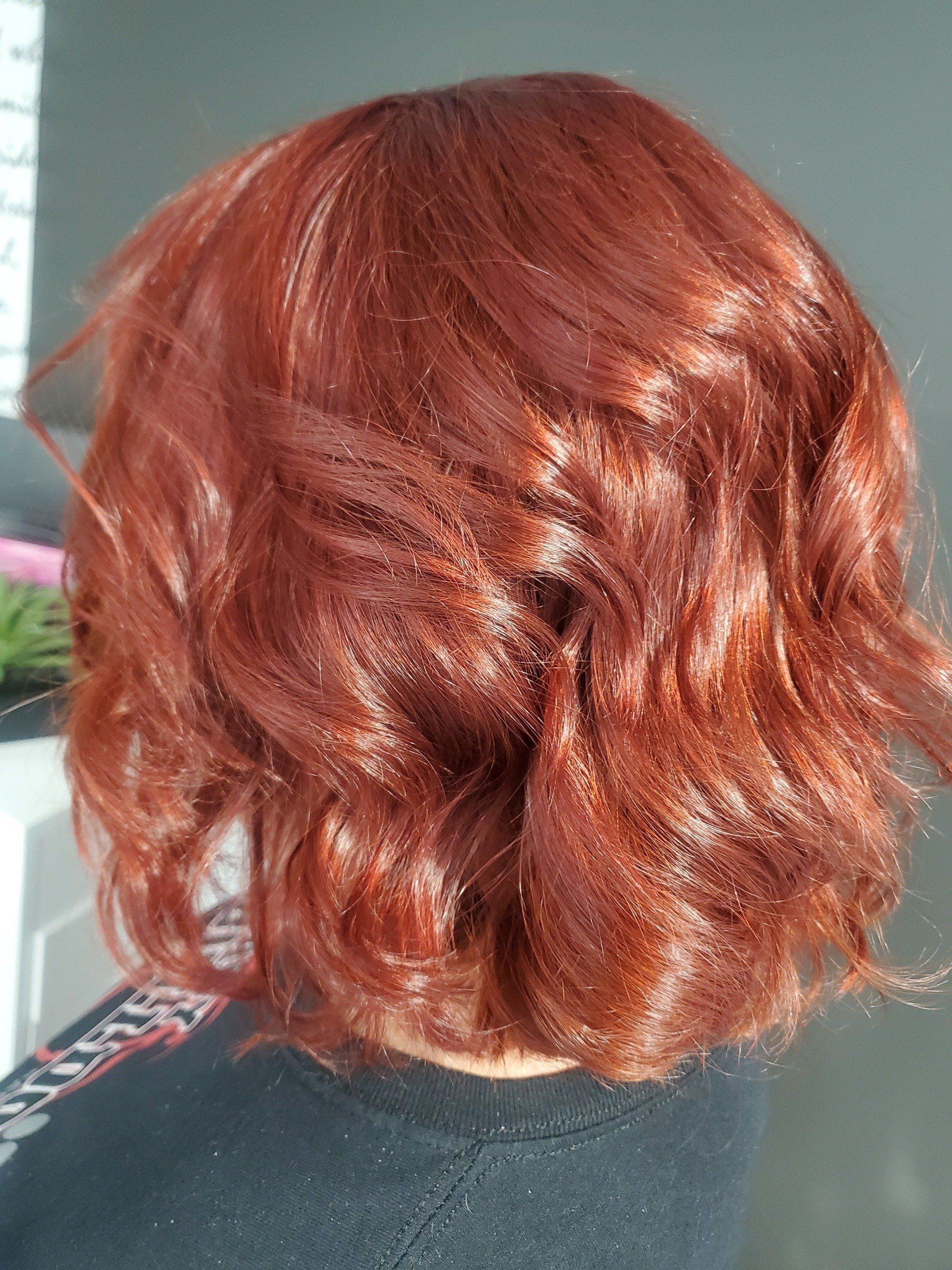 Red wavy hair, close-up, outdoors. Sunlight catches the vibrant color, styled in soft waves.