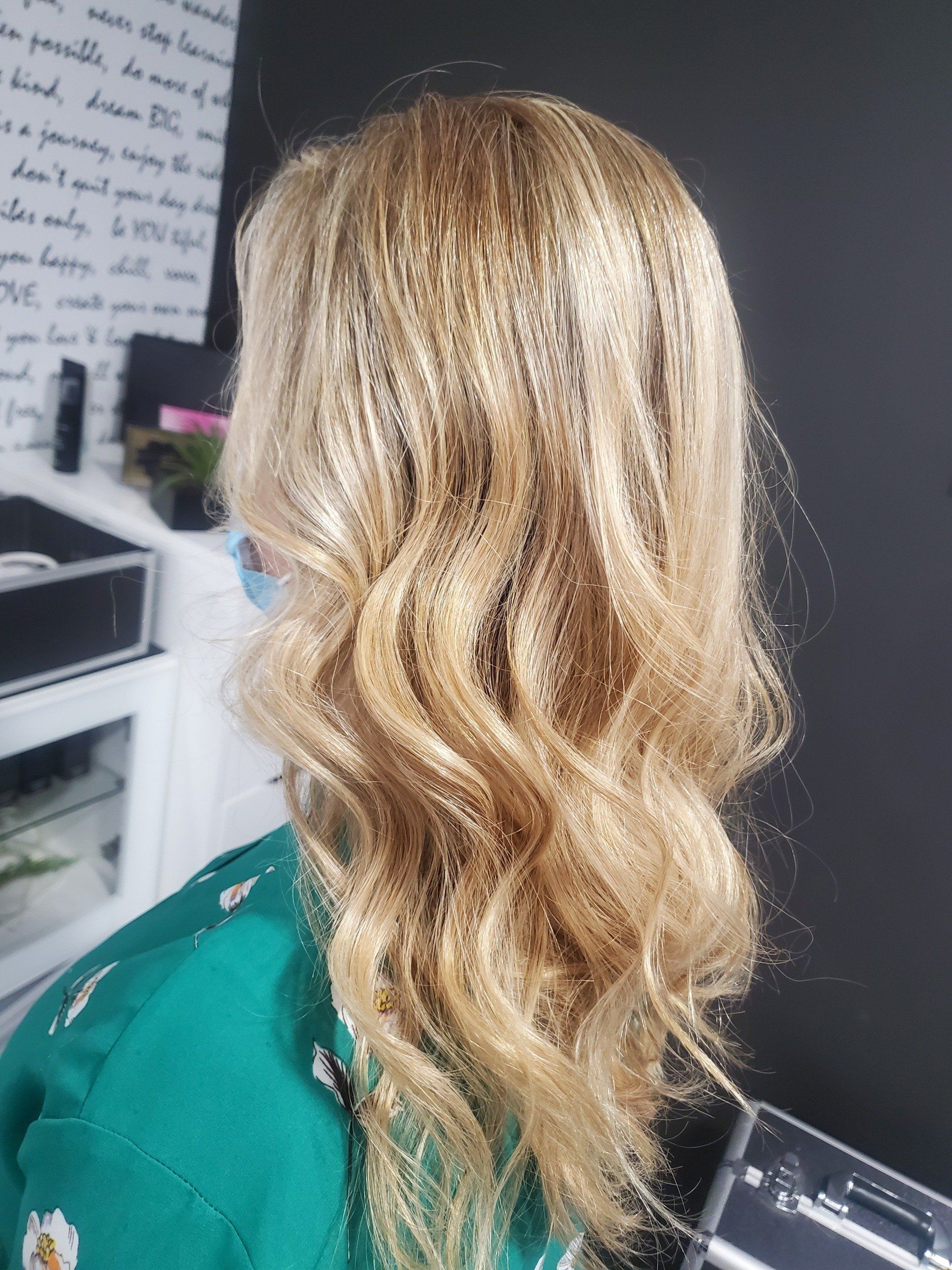 Woman with wavy, blonde hair, wearing a green top, in a salon setting.