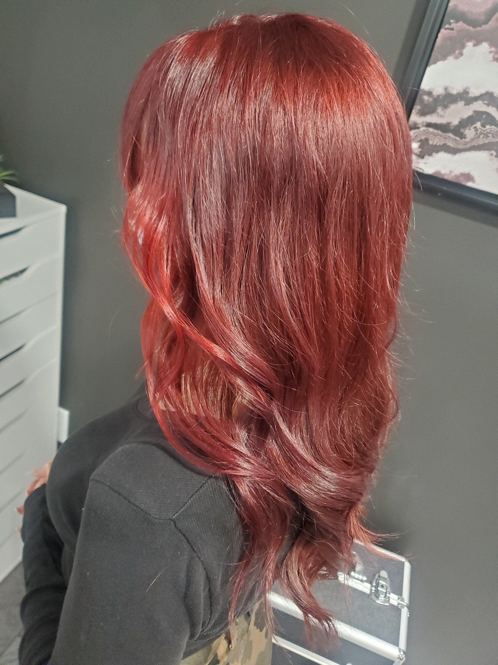 Person with long, shiny, red hair. Half-body shot. They are wearing a black sweater. Gray background.