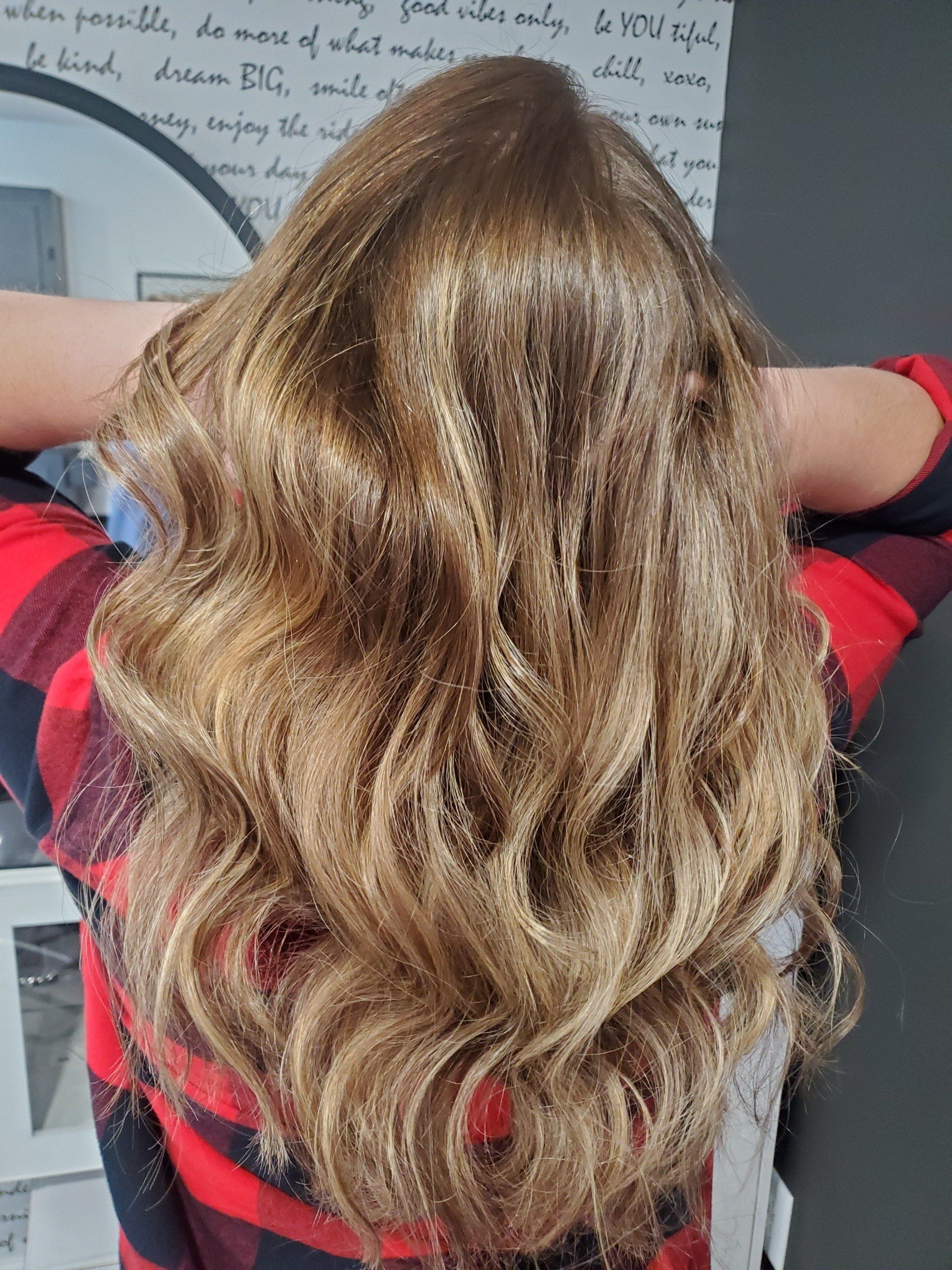 Long wavy blonde hair, styled with loose curls. Person wearing a red and black plaid shirt.