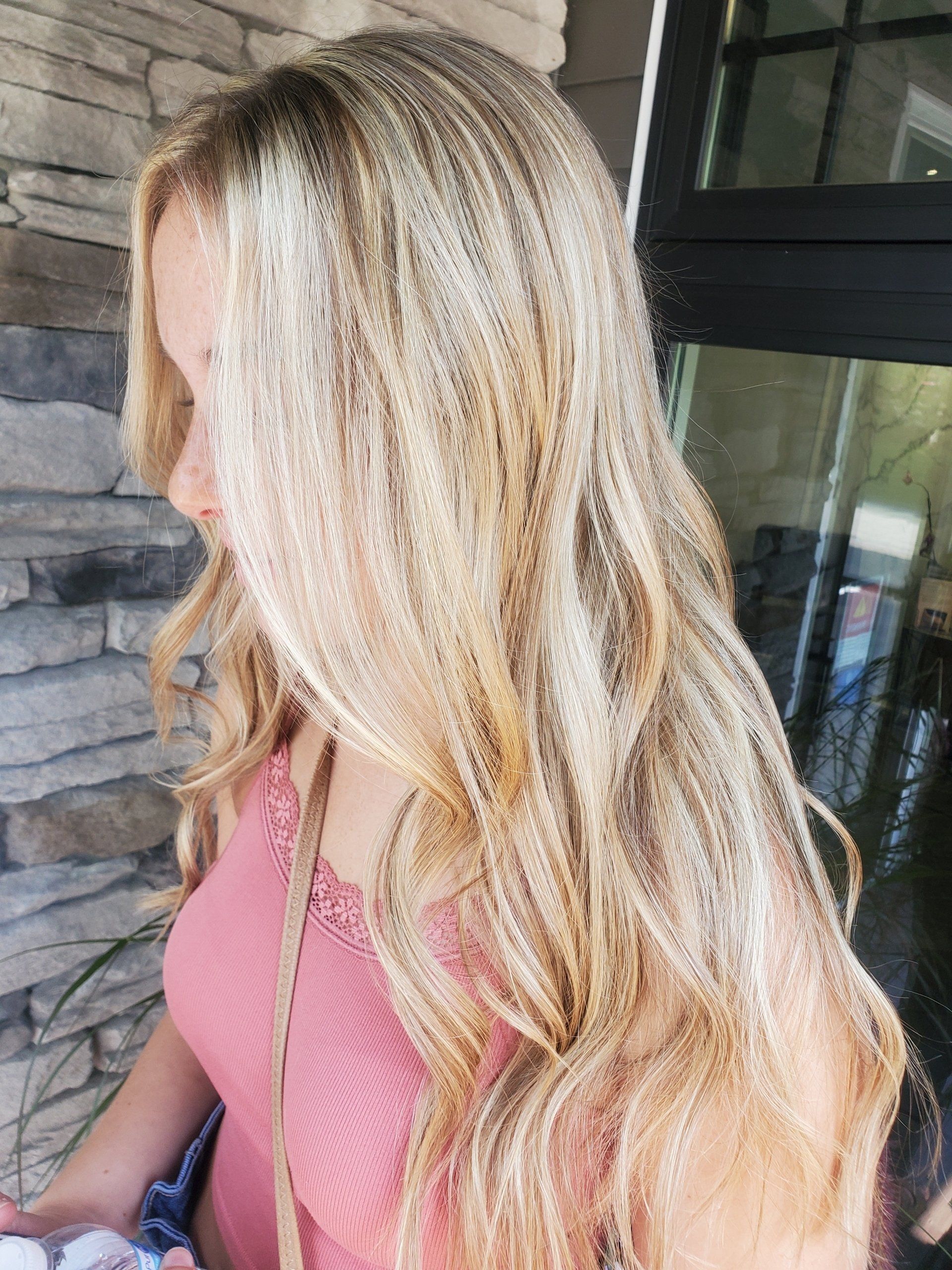 Blonde hair cascading down a pink top, slightly blurred, against a building.