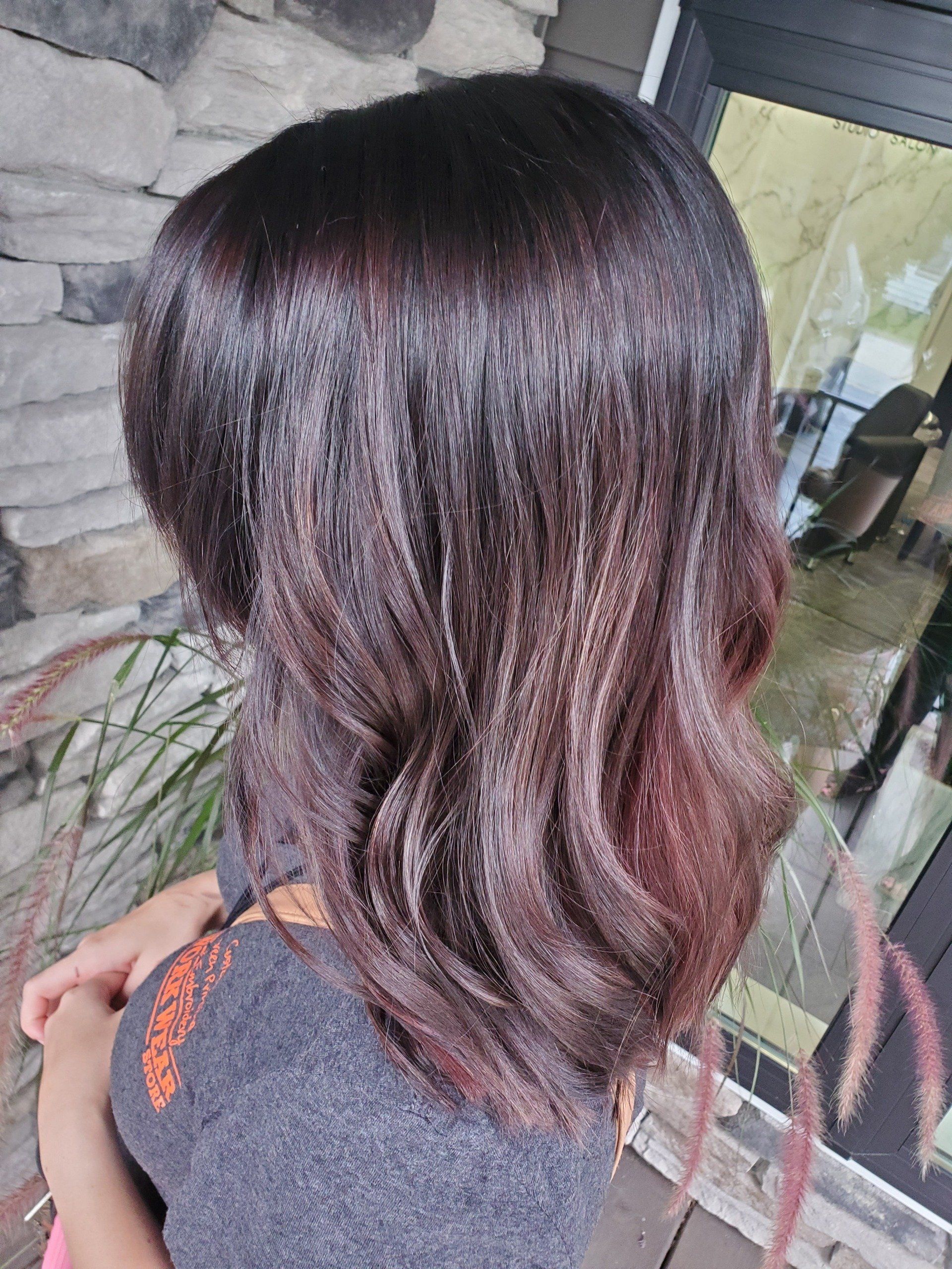 Woman with dark, layered, wavy hair, with red highlights in sunlight.