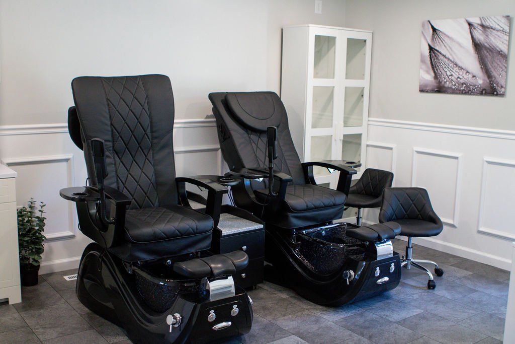 Two black pedicure chairs in a salon setting, with a white cabinet and wall art.