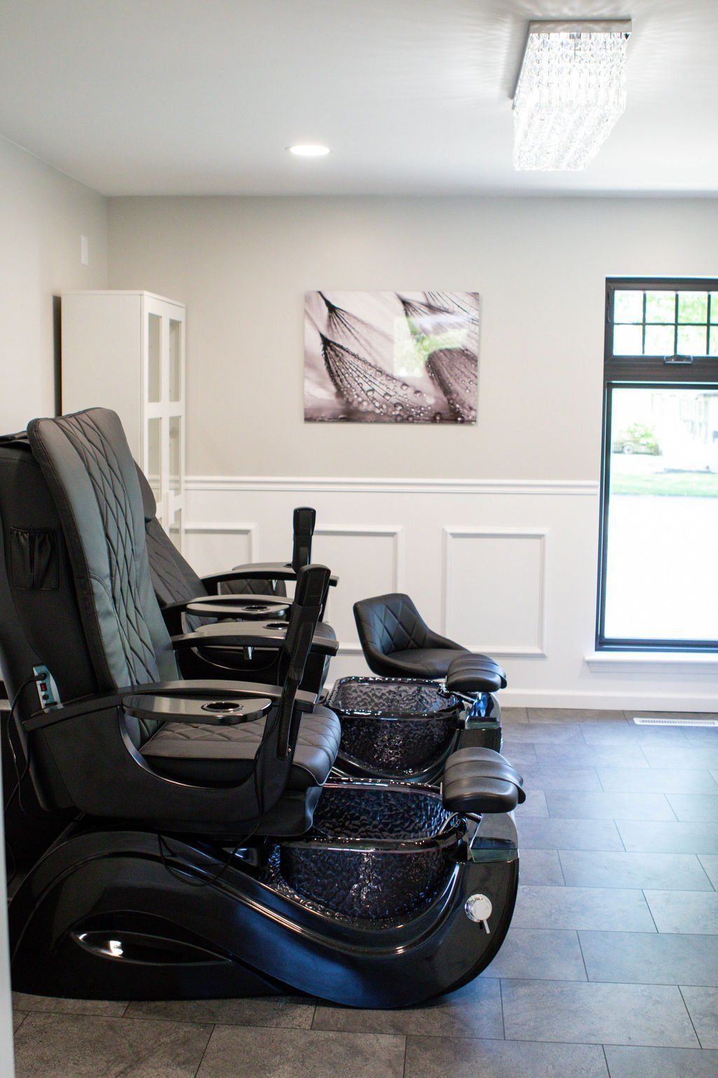 Pedicure station in a spa. Black massage chairs with foot basins, neutral walls, and art.