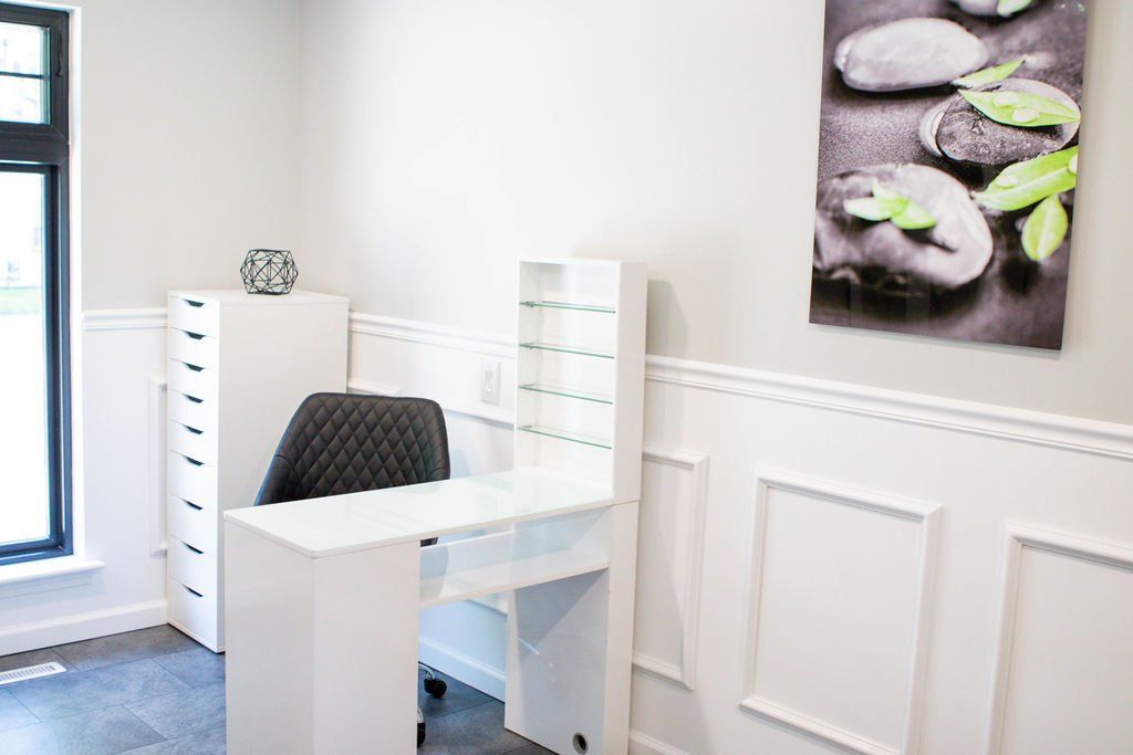 White nail salon with a desk, storage, art, and a chair.