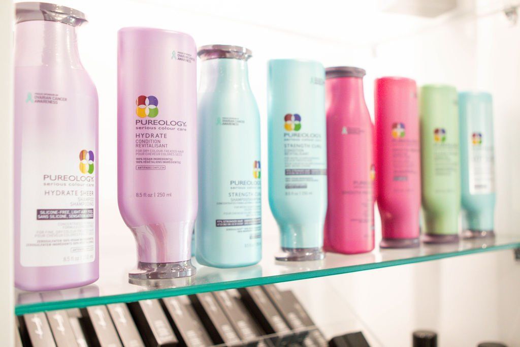 Bottles of colorful hair products on a glass shelf.