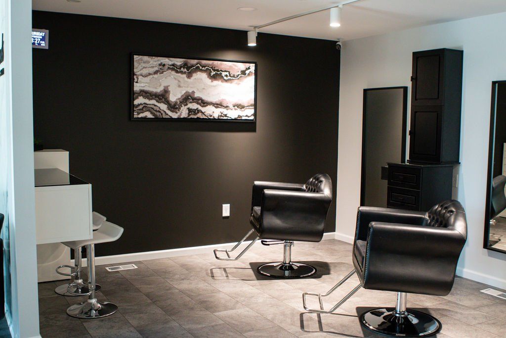 Hair salon interior: black chairs, dark walls, mirrors, artwork, neutral flooring.